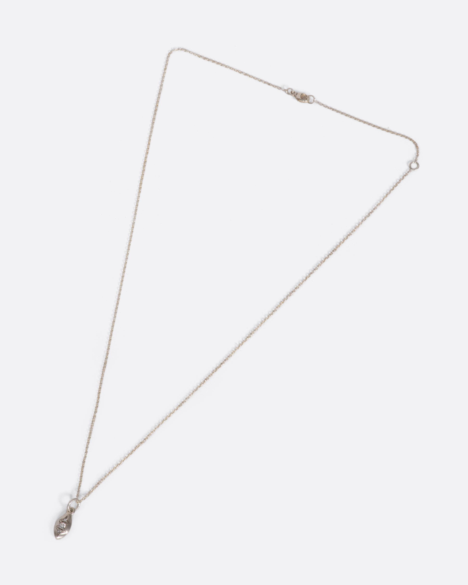 A silver cable chain necklace with a seed shaped pendant with three diamonds and oxidized etching. Shown closed lying flat from the front.