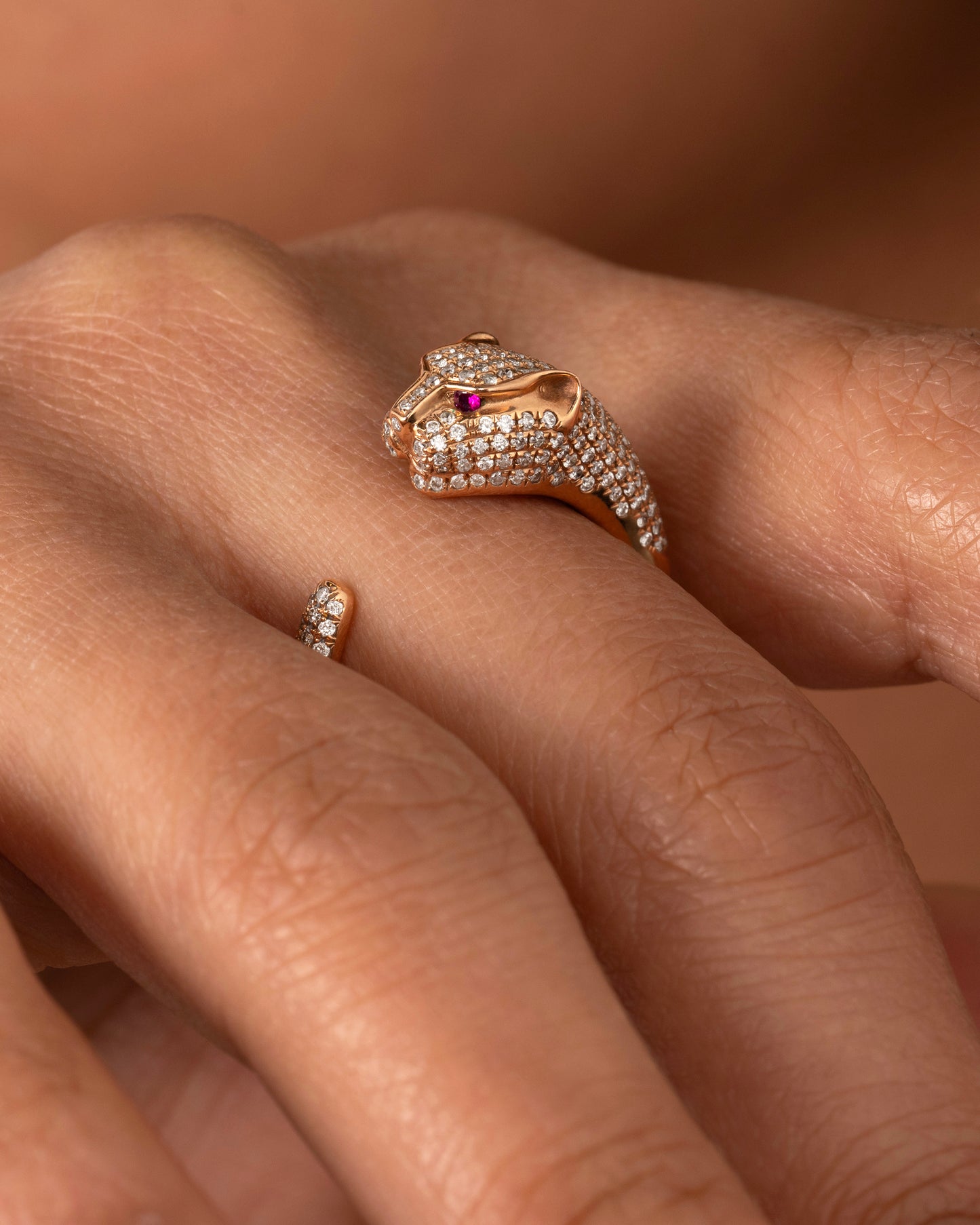 A rose gold panther wrap ring with pave diamonds on the head and tail and ruby eyes. Shown worn on a hand.