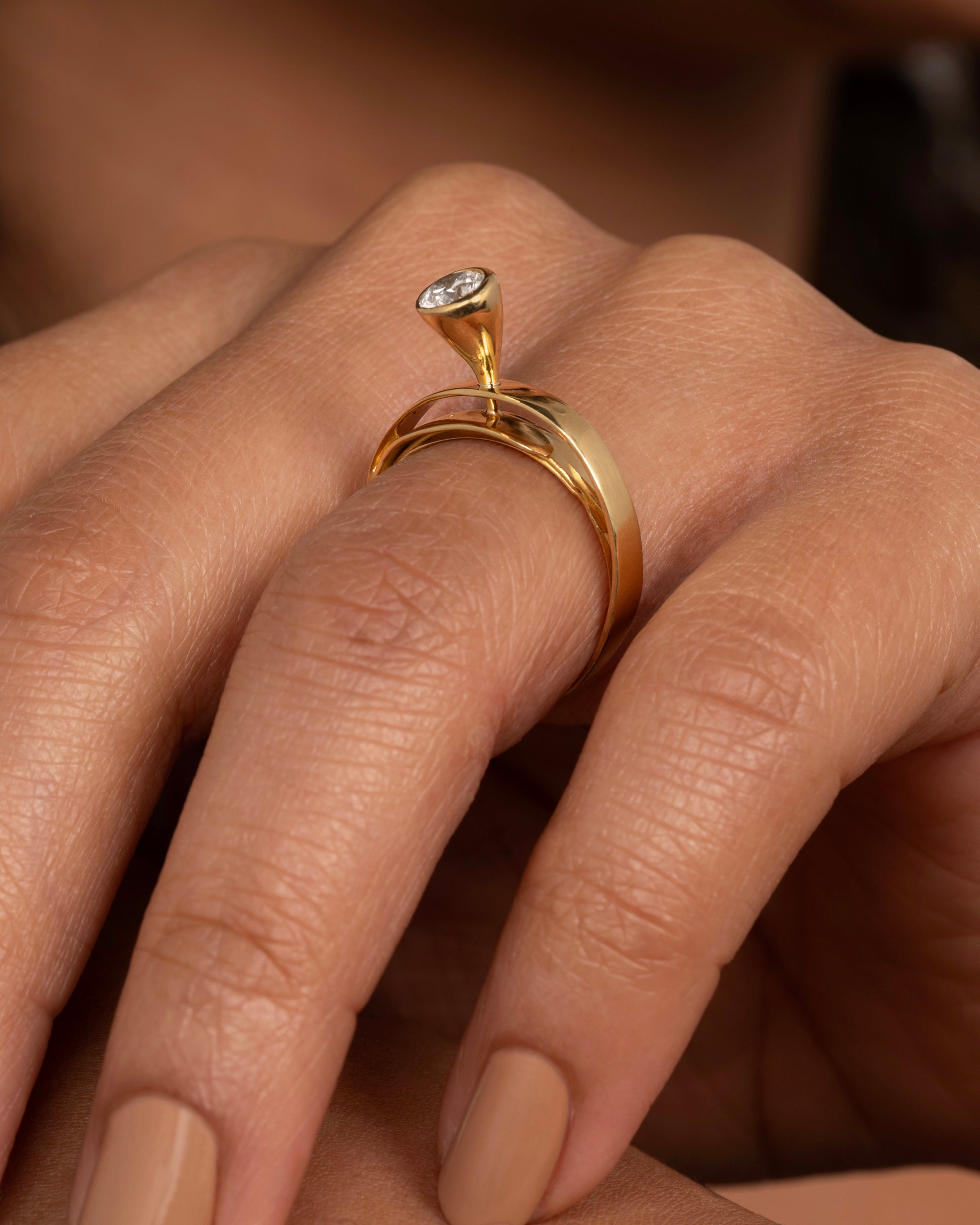 A yellow gold ring that loops over itself twice with a tall bezel set diamond at its center. Shown from the side on a person.