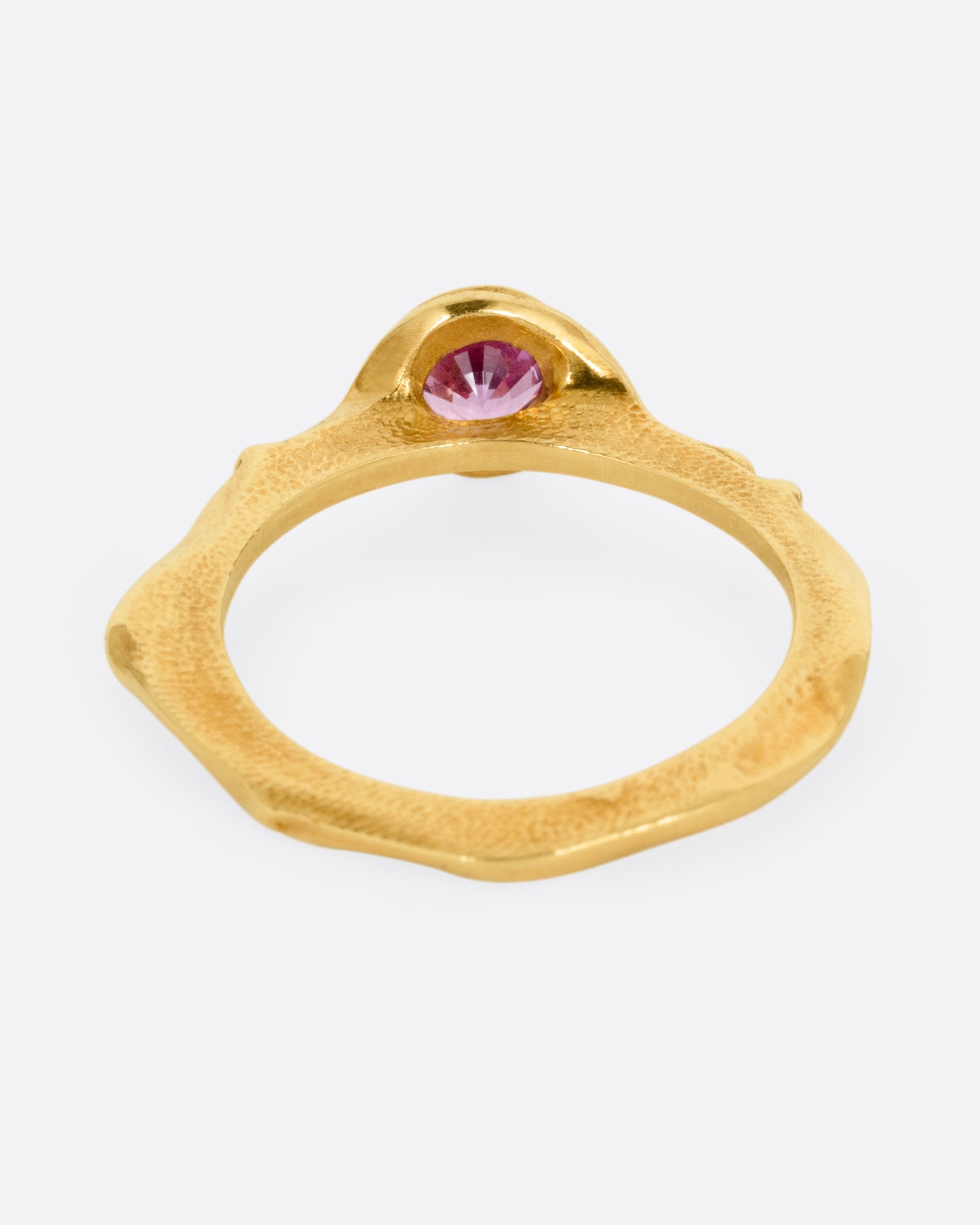 A yellow gold narrow sculptural ring with a purple sapphire, shown from the back.