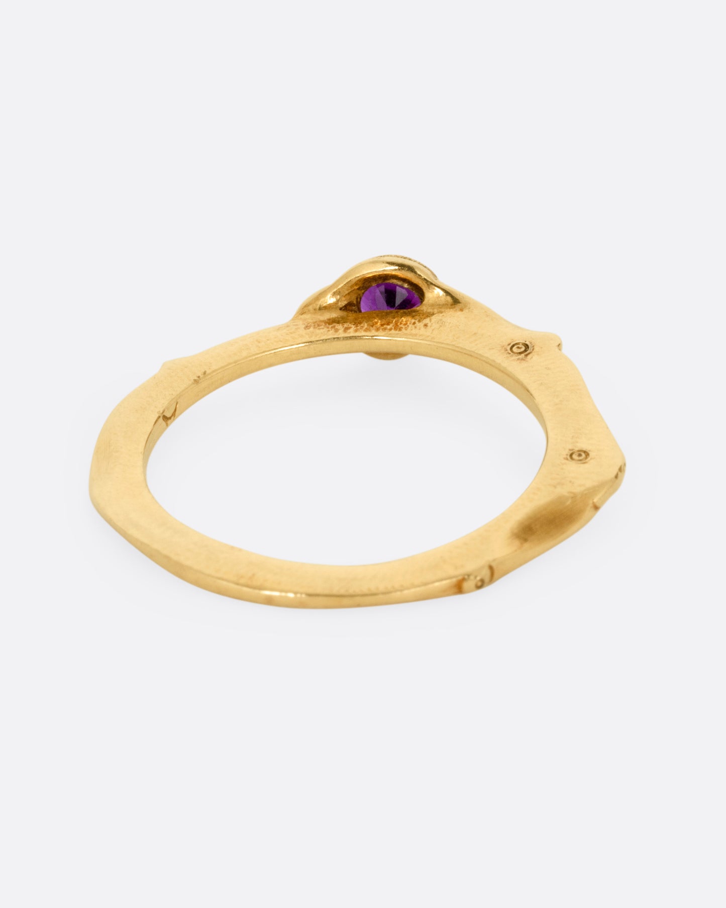 A yellow gold narrow sculptural ring with a purple sapphire, shown from the back.