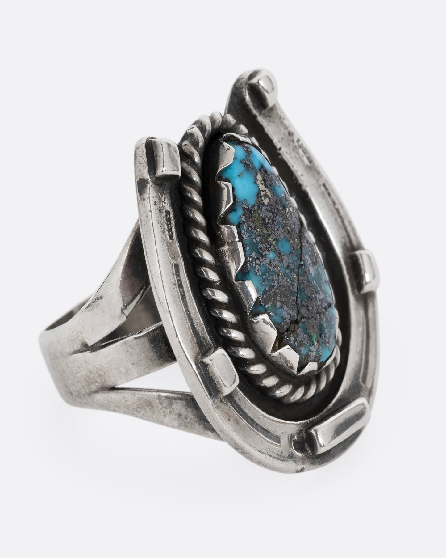 A silver horseshoe ring with a free- form turquoise in the center. Shown from the side.