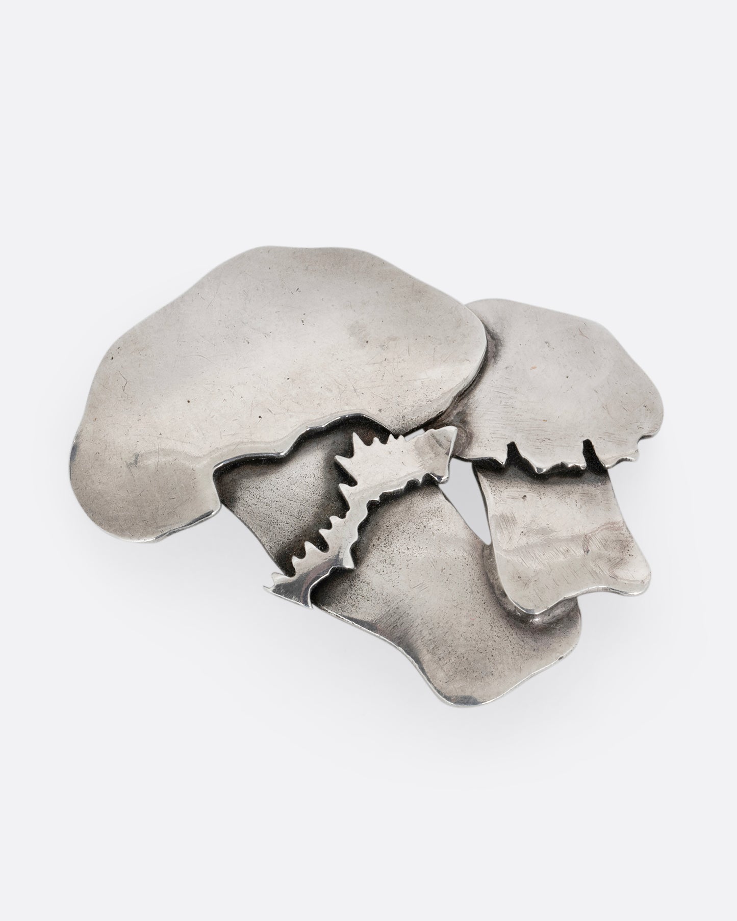A silver pin with two mushrooms. Shown from the front.