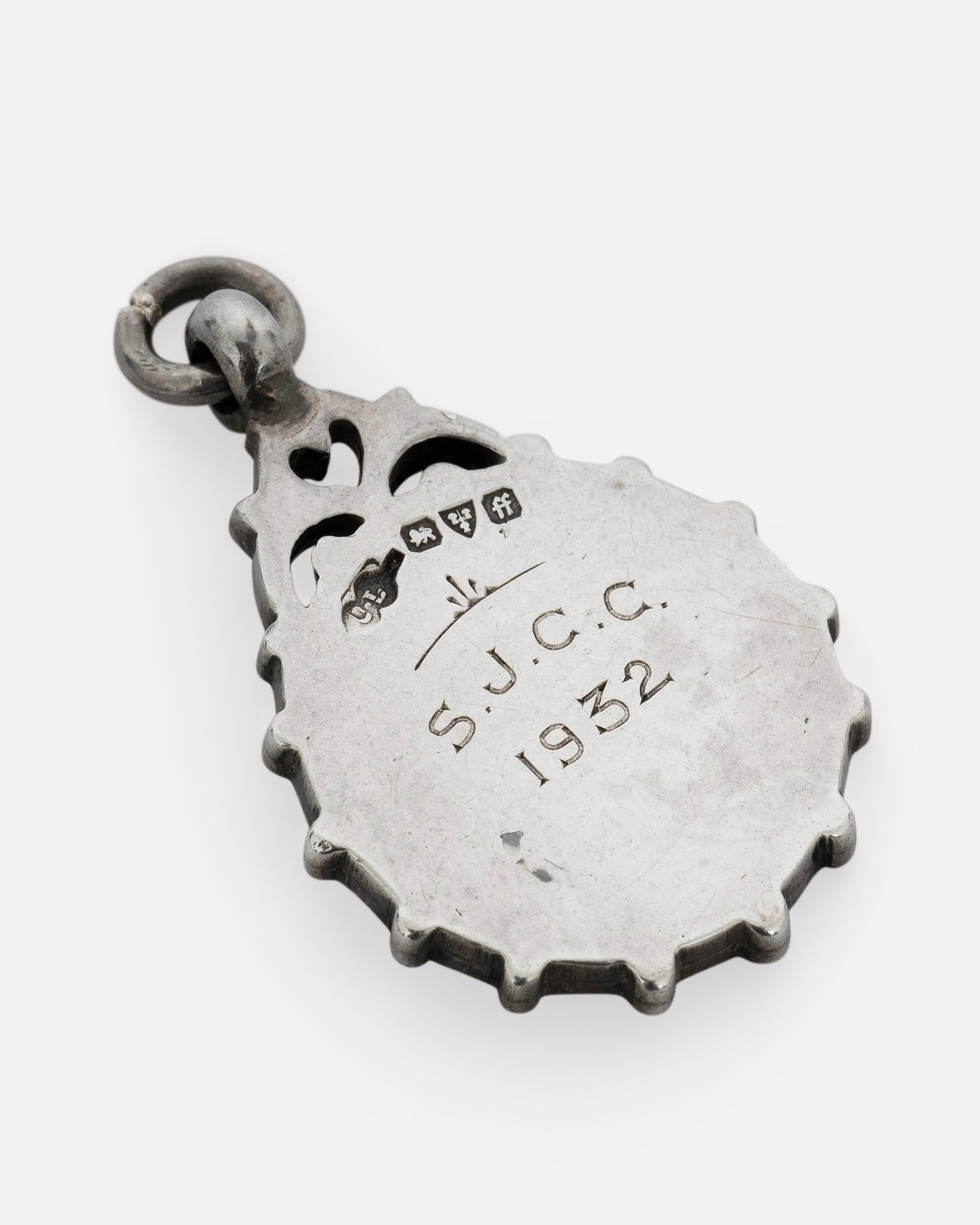 A round silver pendant with S.J.C.C. 1932 engraved in the center. Shown from the back.