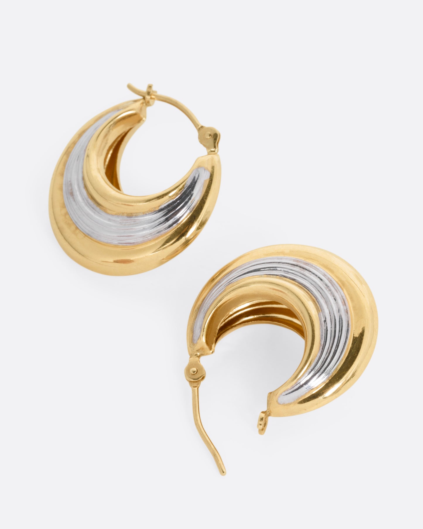 A pair of yellow gold and silver hoop earrings, shown lying on their sides with one earring open.