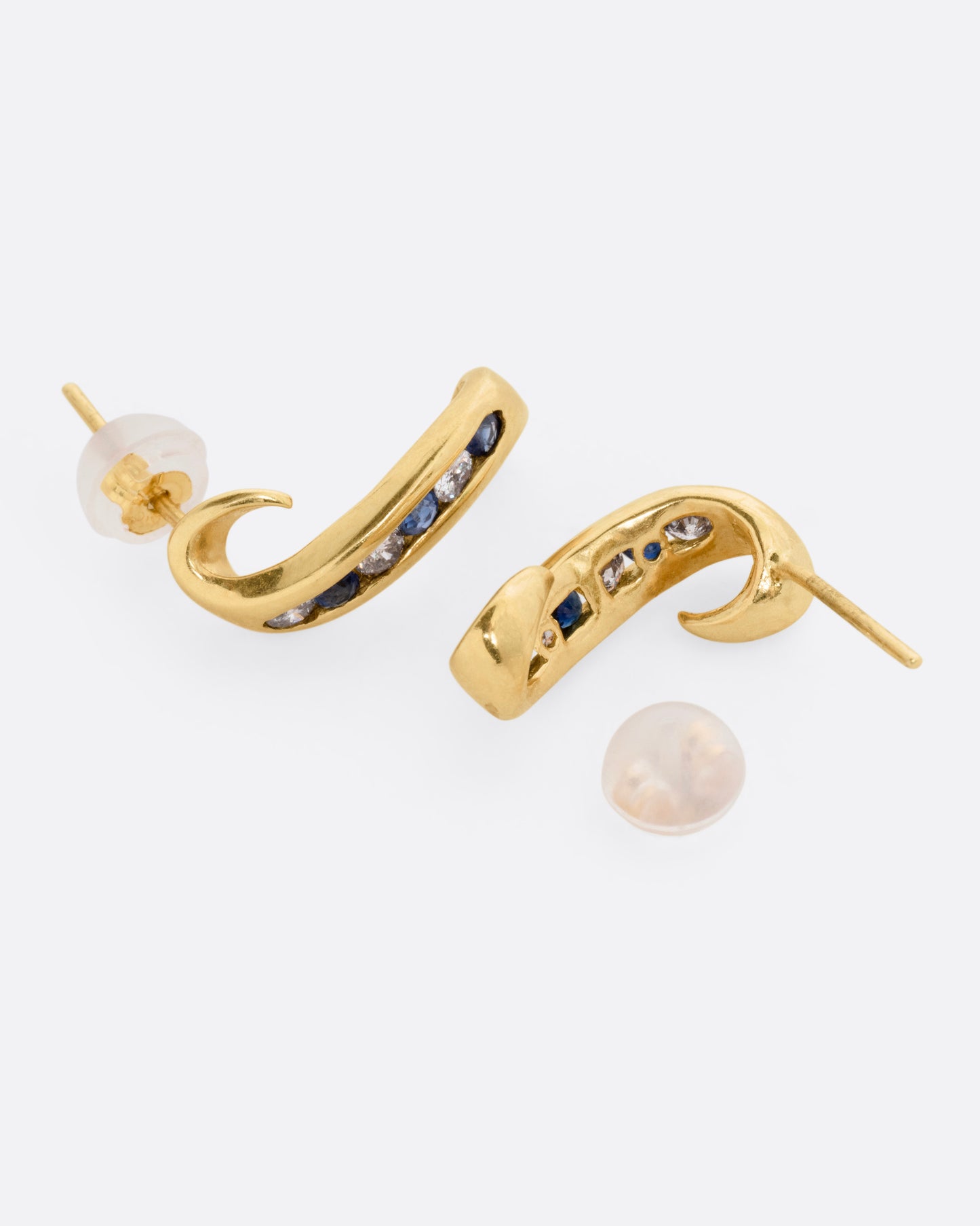 A pair of yellow gold scroll shaped earrings with a queue of channel set diamonds and sapphires, shown on their sides with one earring open.