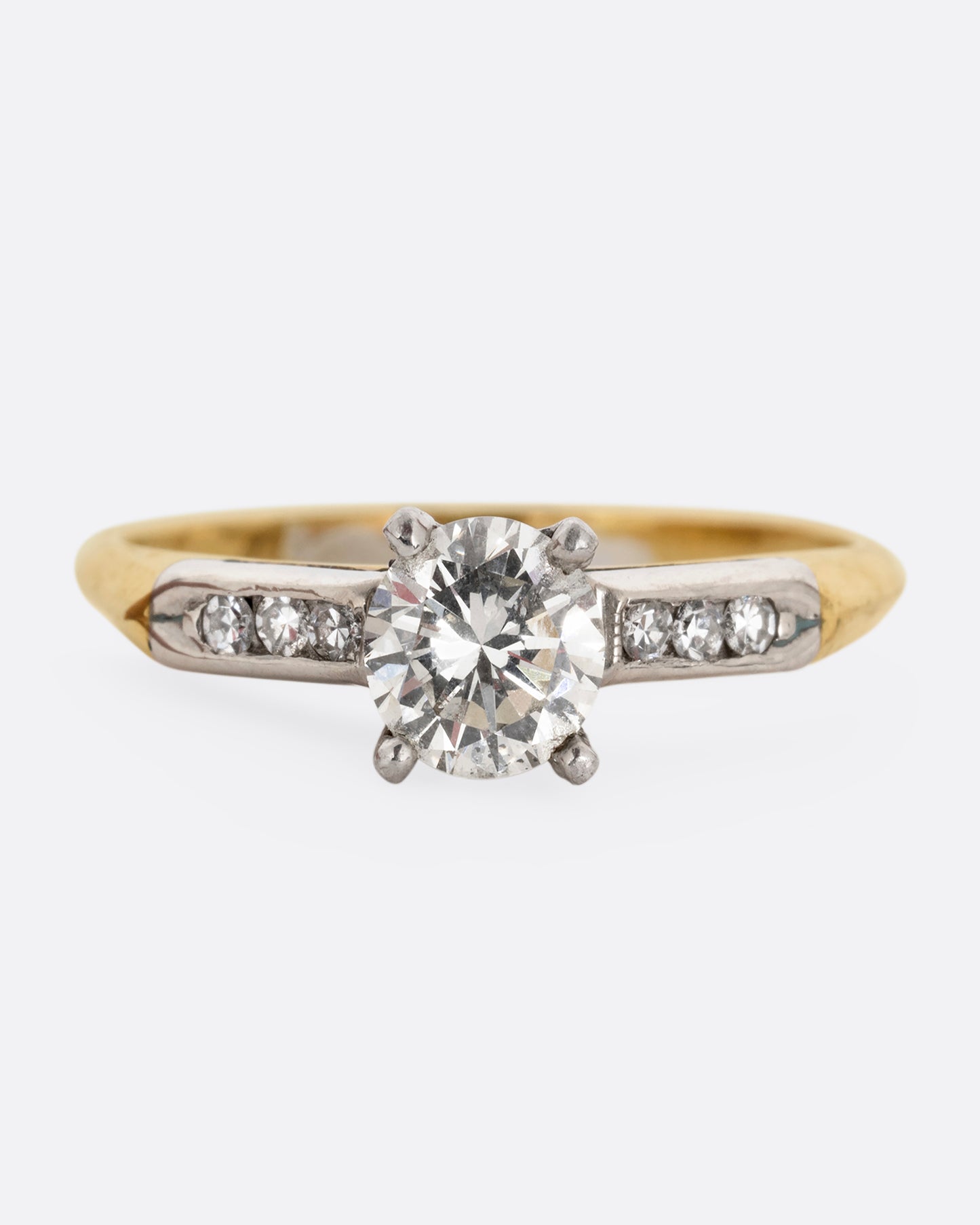 A yellow gold ring with white gold setting and six channel set diamonds with a central prong set brilliant cut diamond. Shown from the front.