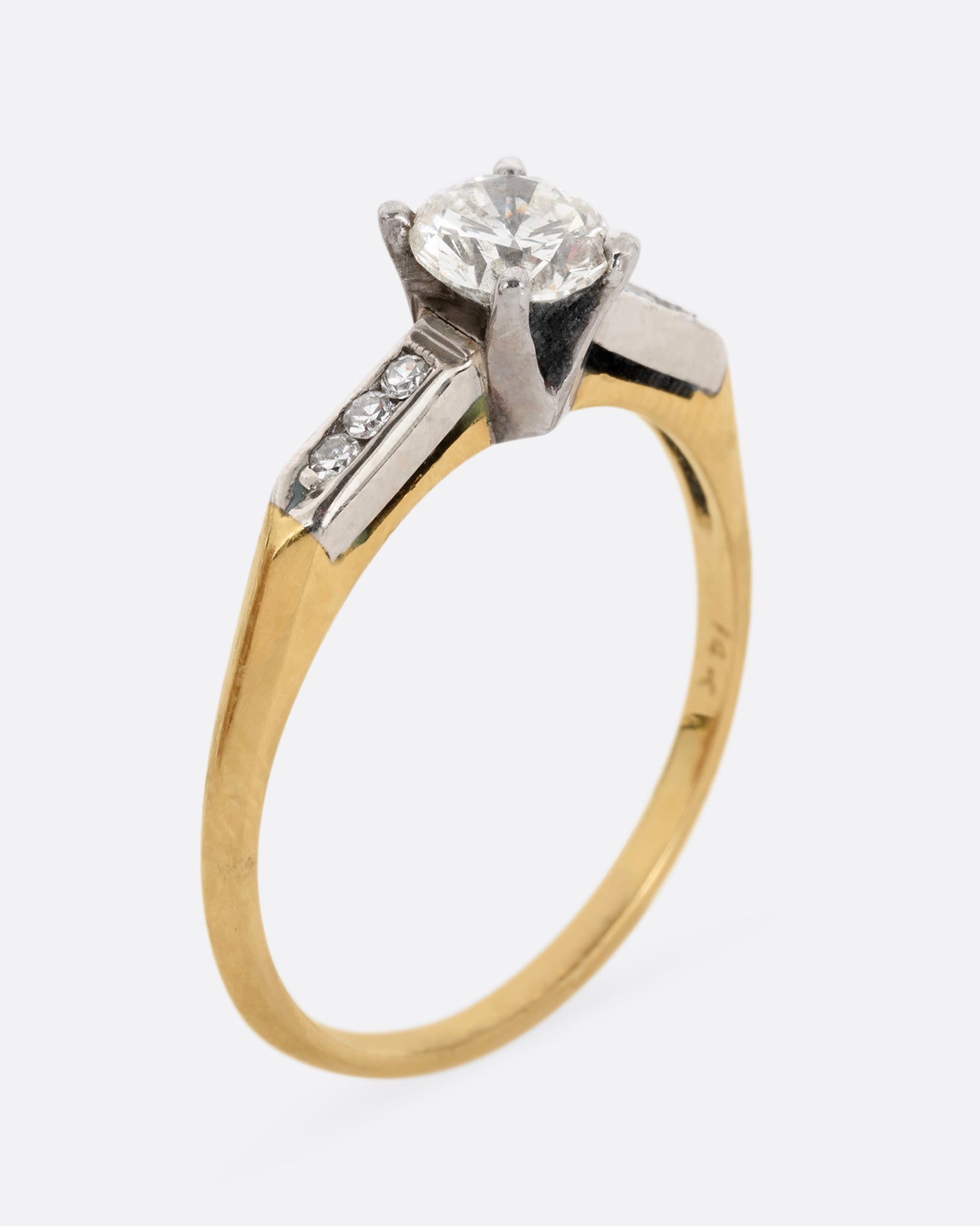 A yellow gold ring with white gold setting and six channel set diamonds with a central prong set brilliant cut diamond. Shown standing up from the side.