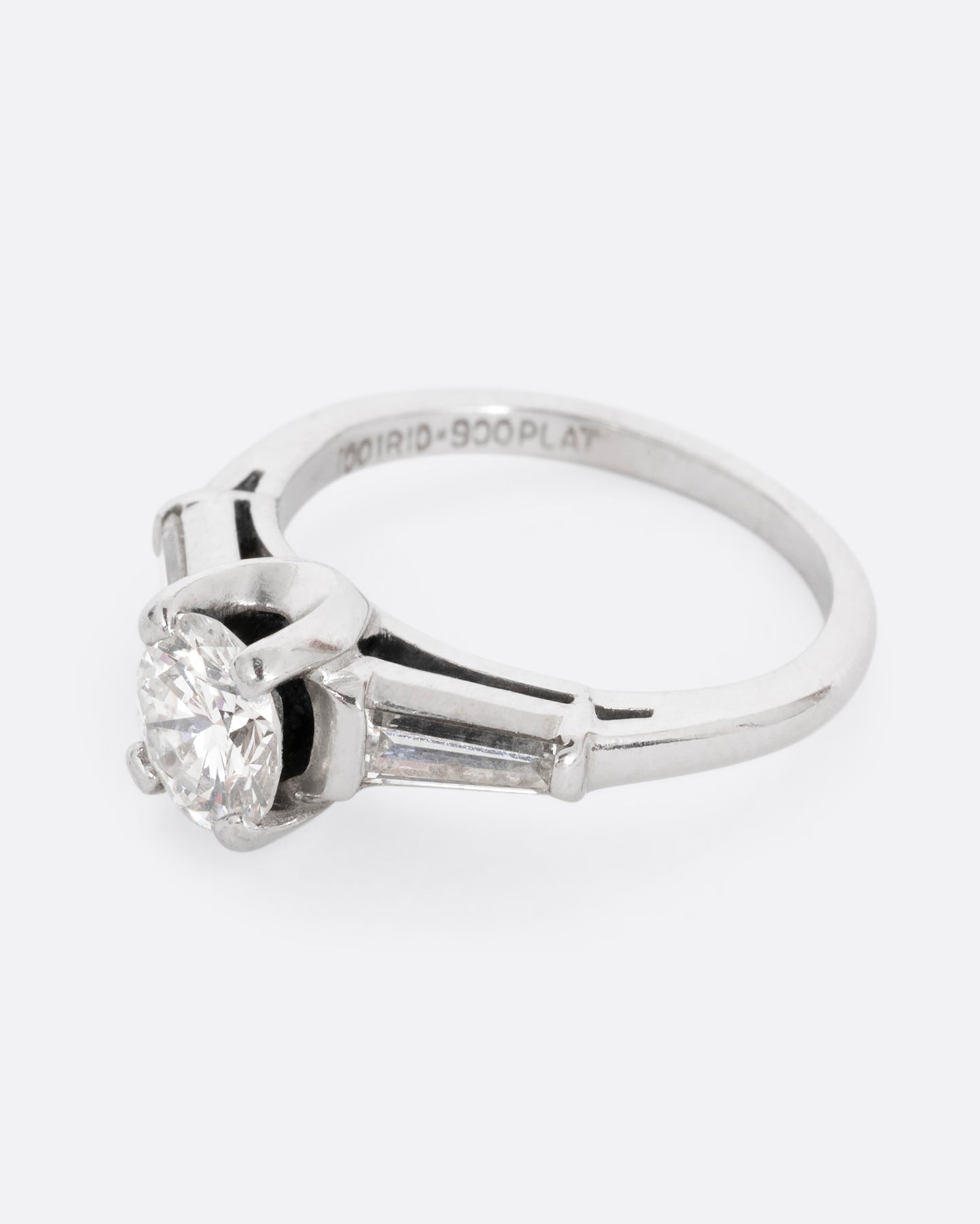 A platinum ring with a brilliant cut prong set diamond and two baguette diamonds. Shown from the side.