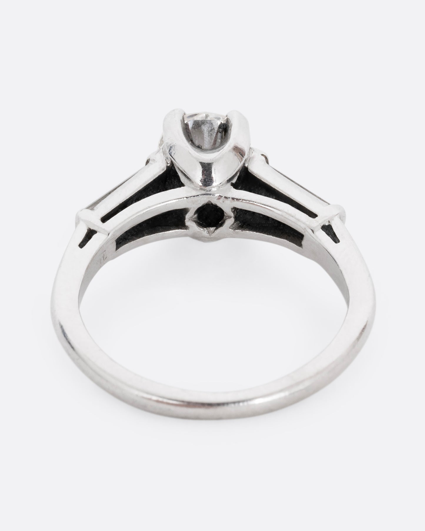 A platinum ring with a brilliant cut prong set diamond and two baguette diamonds. Shown from the back.