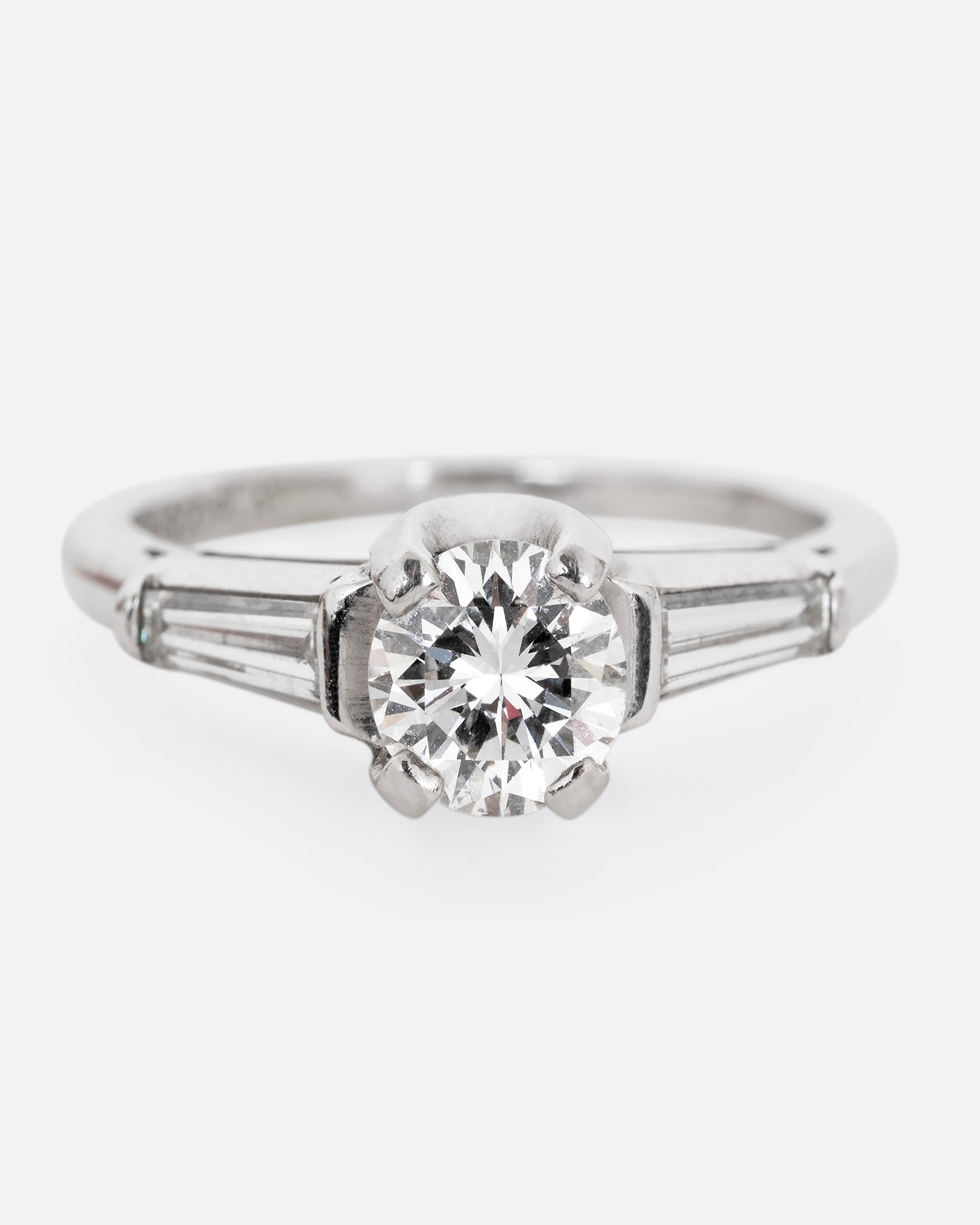 A platinum ring with a brilliant cut prong set diamond and two baguette diamonds. Shown from the front.