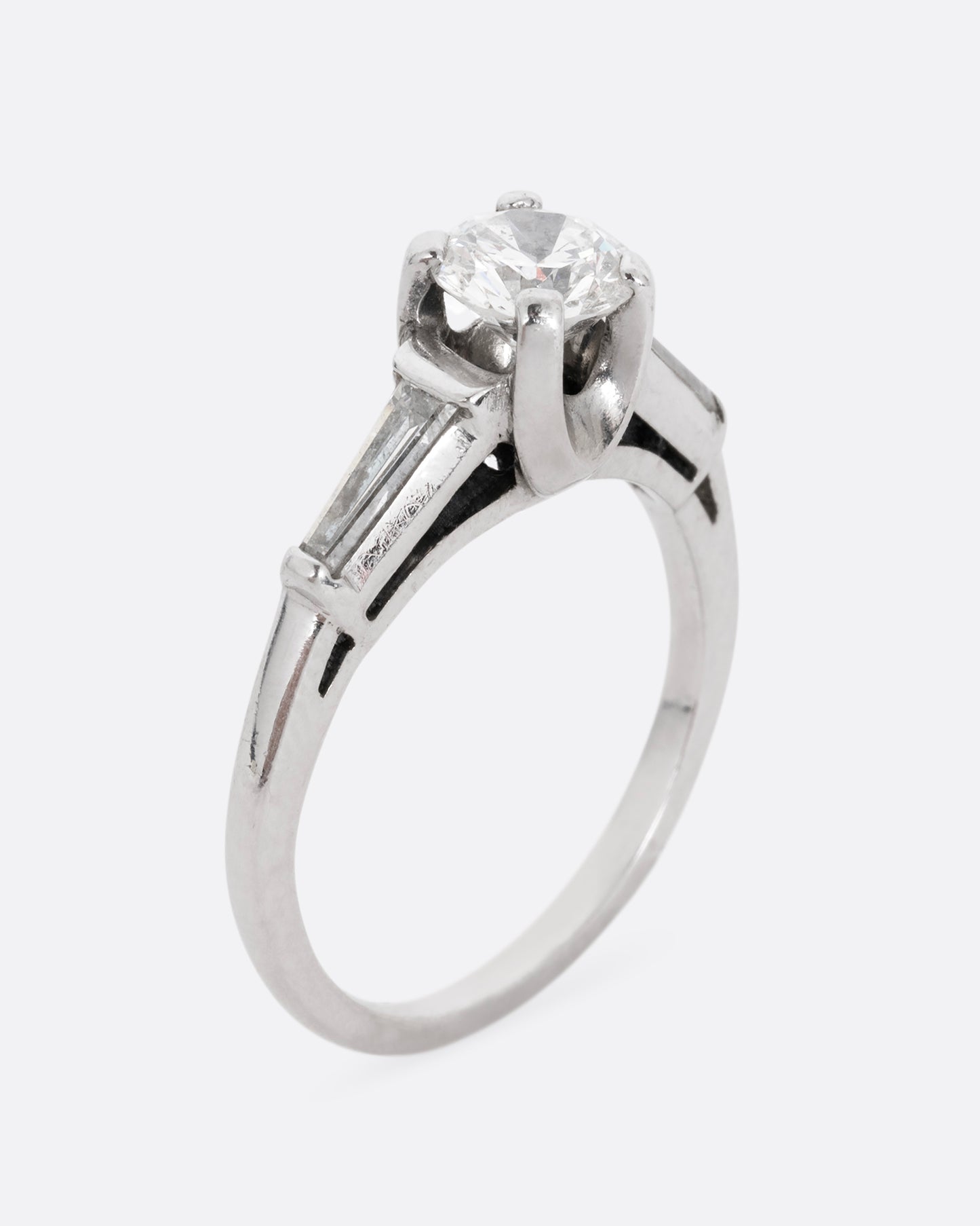 A platinum ring with a brilliant cut prong set diamond and two baguette diamonds. Shown standing up from the side.