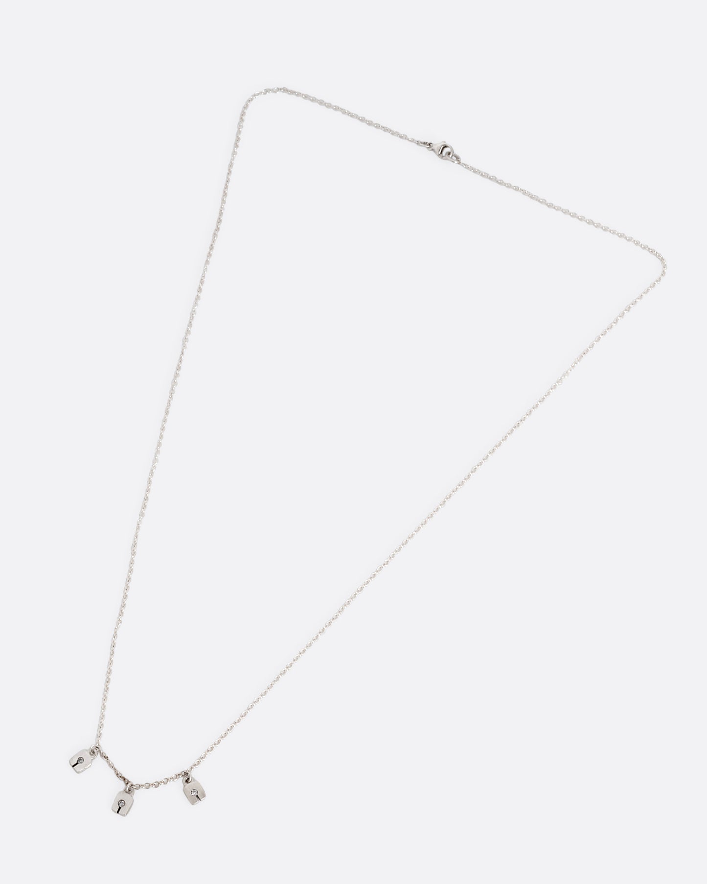 A silver cable chain necklace with three square charms with grey diamonds. Shown clasped lying flat.