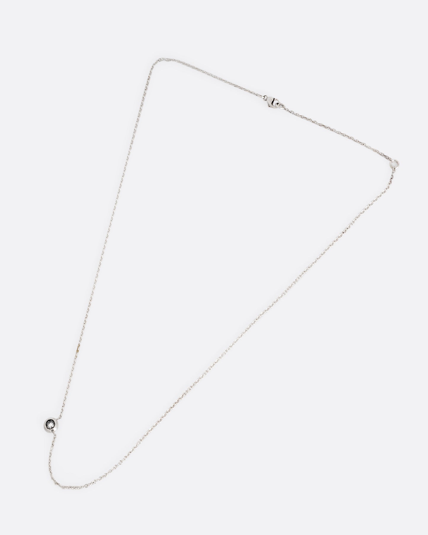 A silver cable chain necklace with a reverse set grey diamond. Shown clasped lying flat.