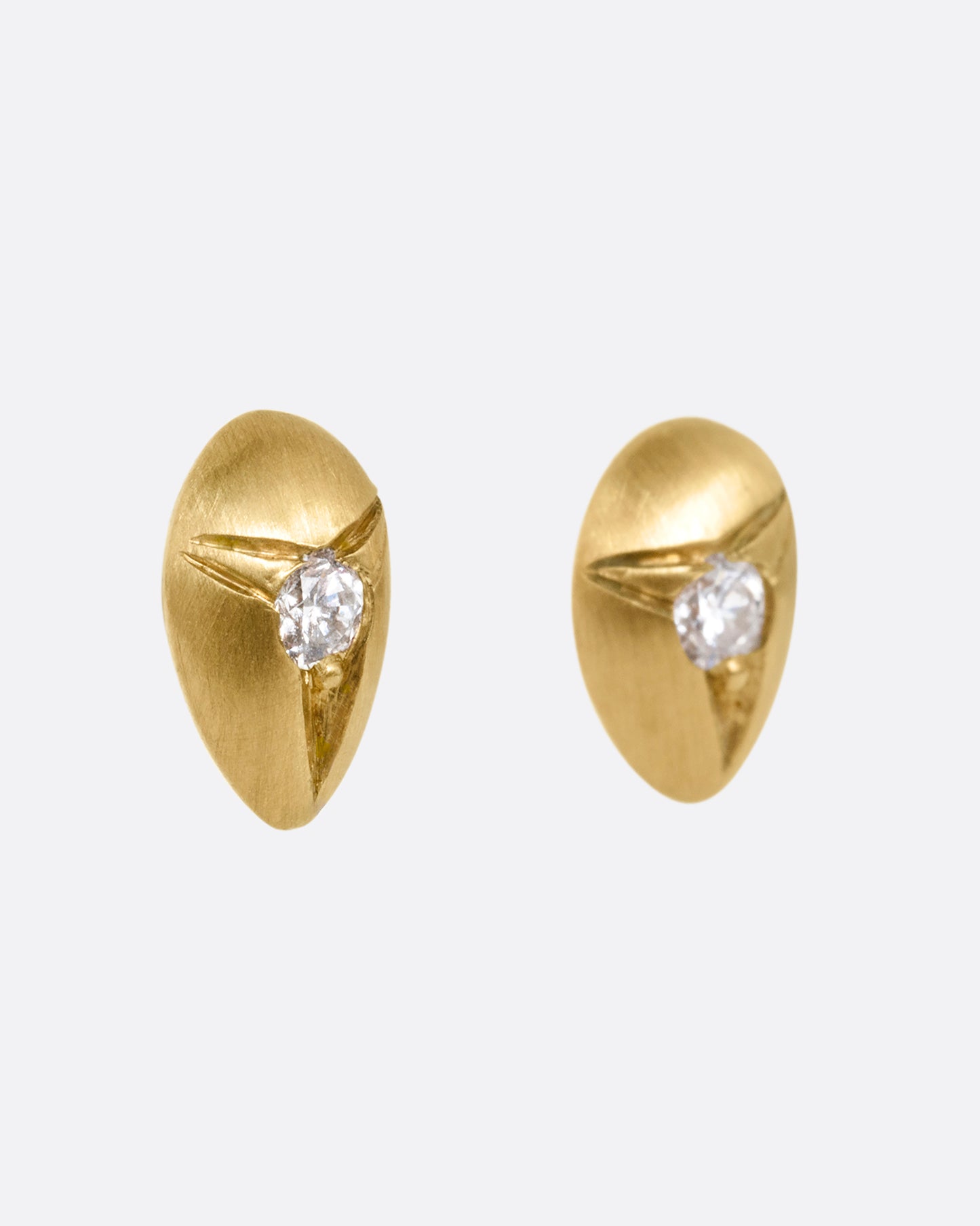 Yellow brushed gold teardrop shaped earrings with white diamonds at the center. Shown from the side.