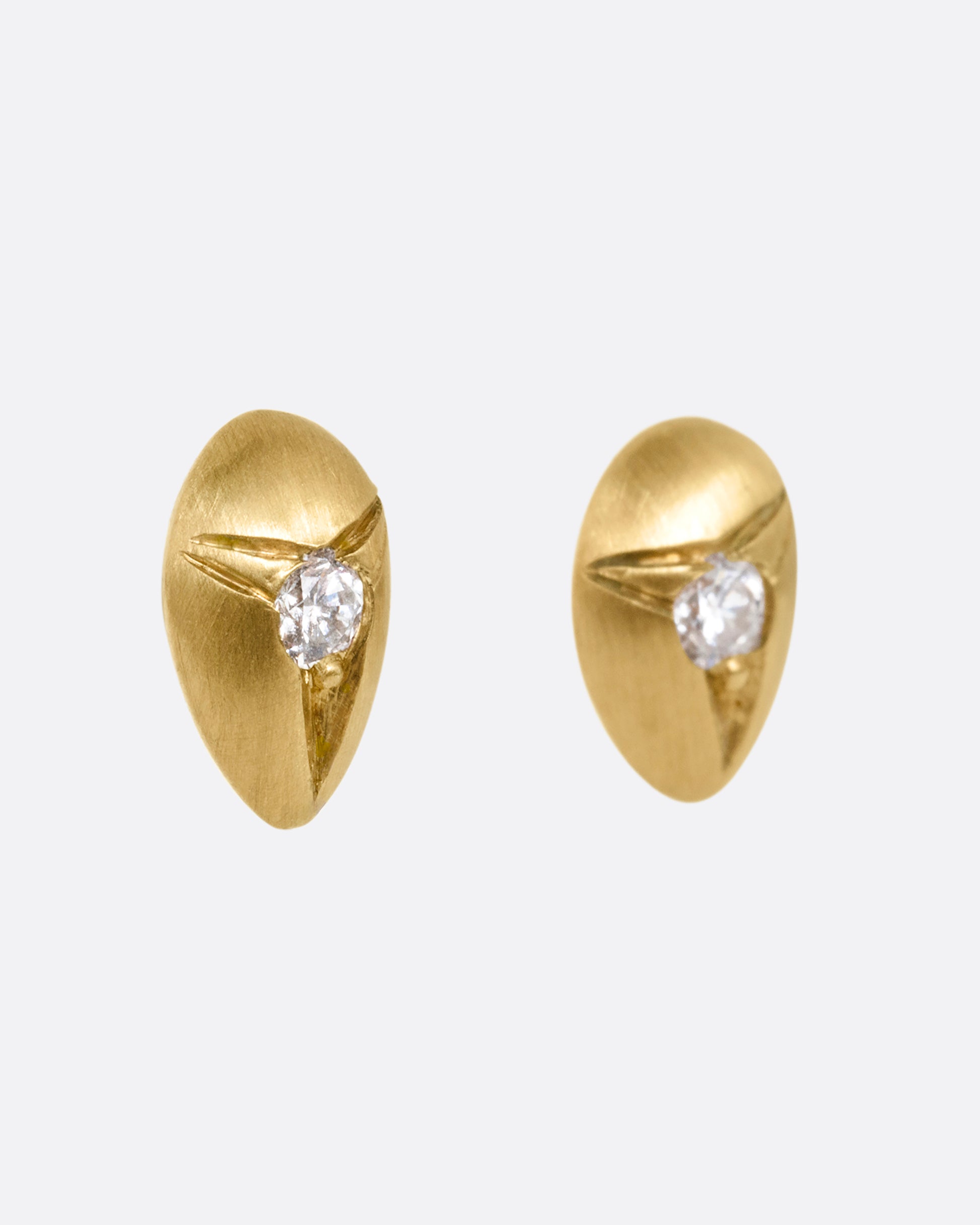 Yellow brushed gold teardrop shaped earrings with white diamonds at the center. Shown from the side.