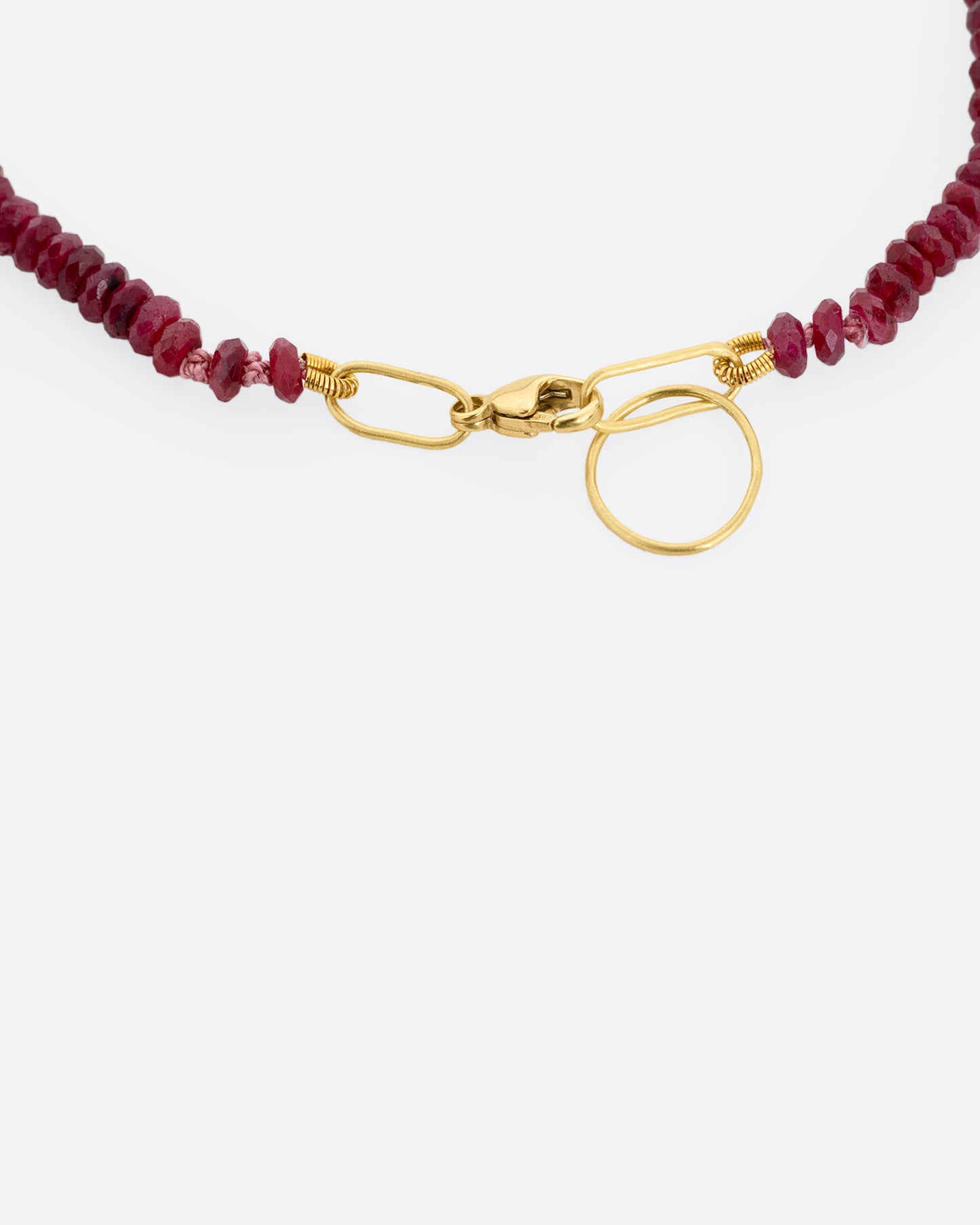 A close up of a beaded ruby bracelet with a yellow gold clasp.