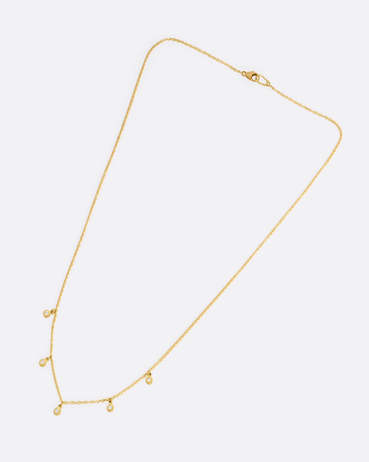 A yellow gold necklace with five brilliant bezel set diamond charms on a cable chain. Shown closed lying flat from the front.