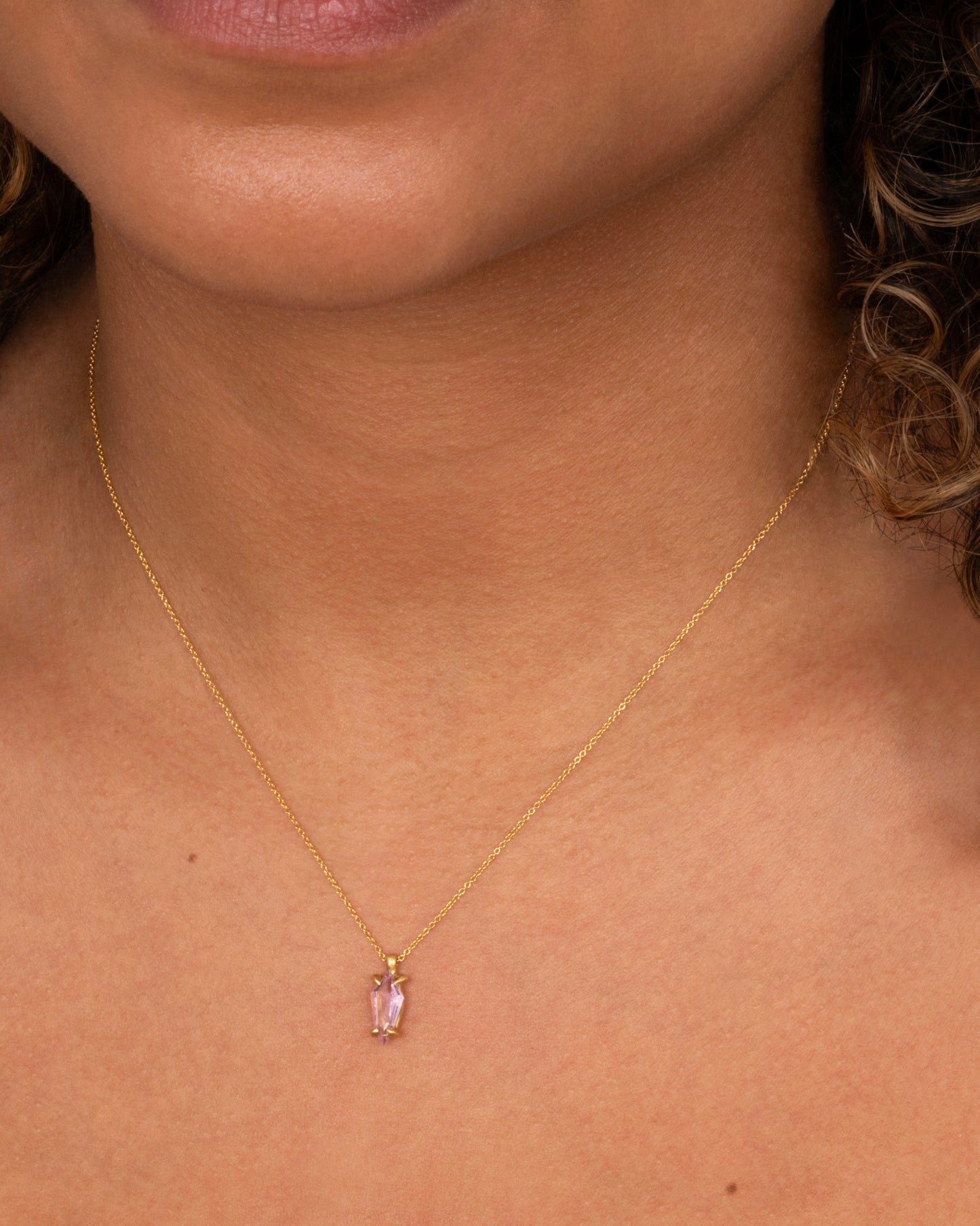 A yellow gold cable chain necklace with a single pink sapphire pendant. Shown worn around a neck.