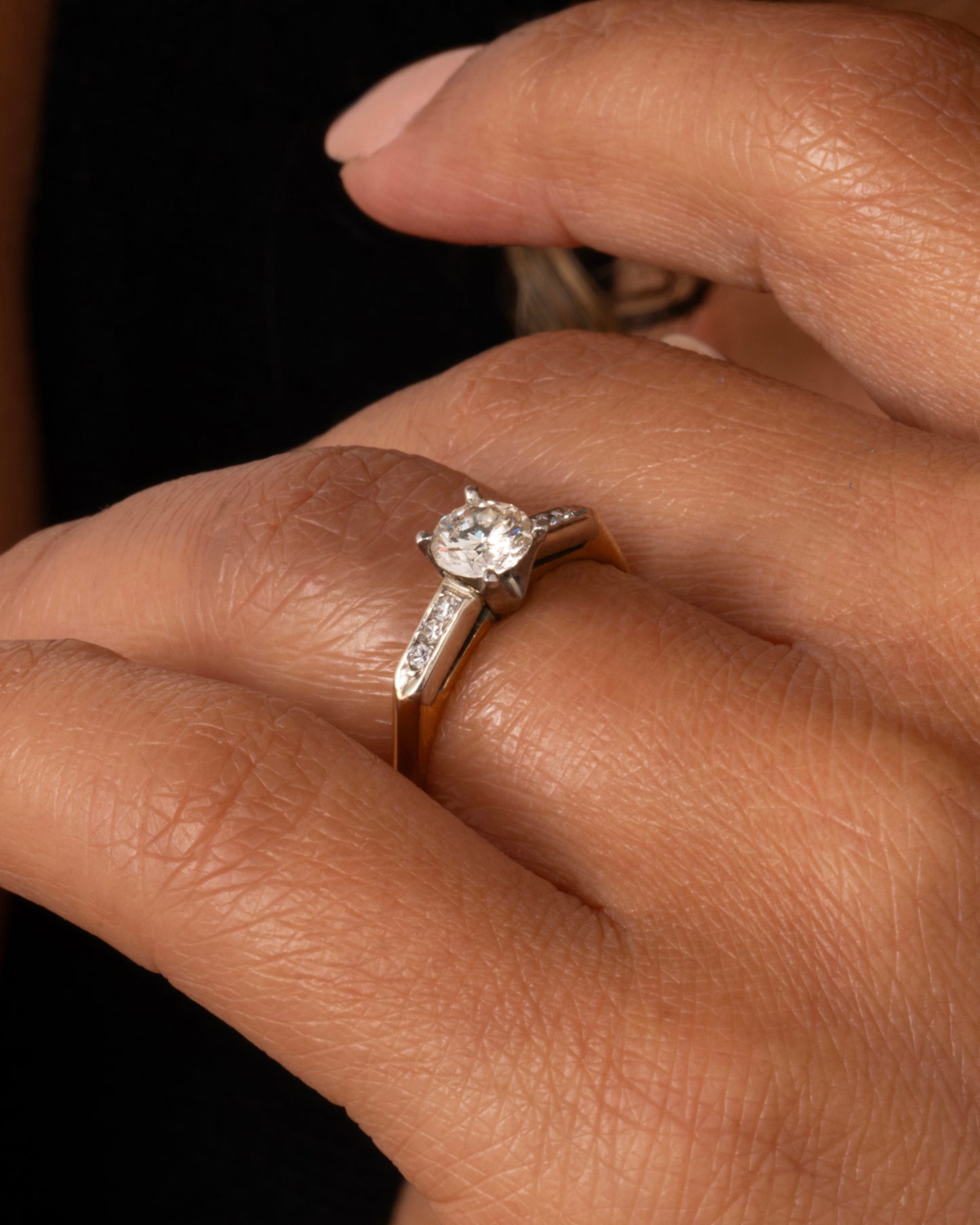 A yellow gold ring with white gold setting and six channel set diamonds with a central prong set brilliant cut diamond. Shown worn on a hand.
