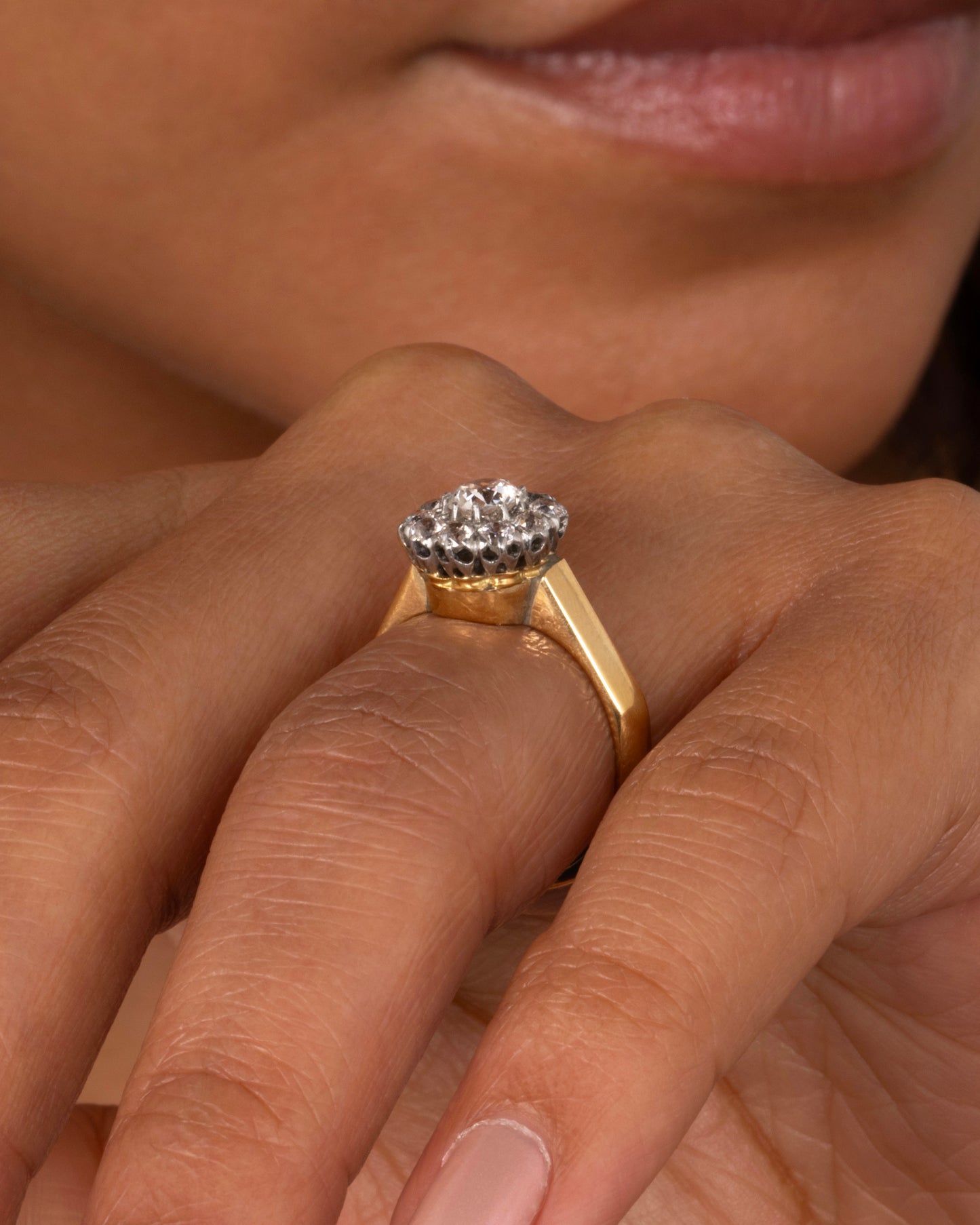 A wide flat yellow gold ring with a flower-shaped cluster of diamonds, shown worn on a hand.