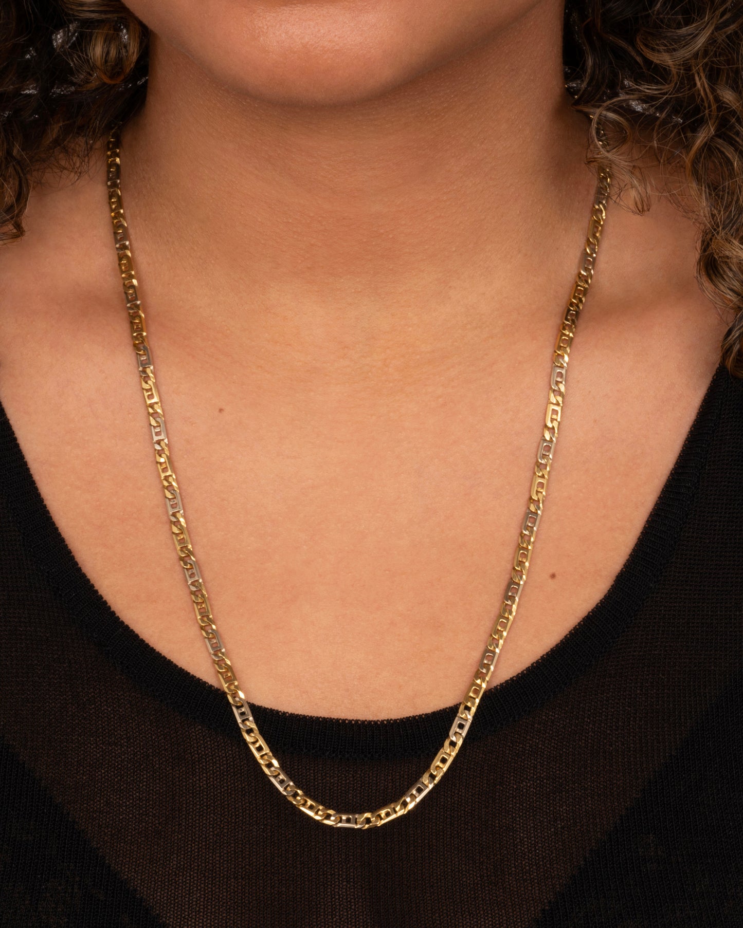 A white and yellow gold geometric flat chain necklace. Shown worn around a neck.