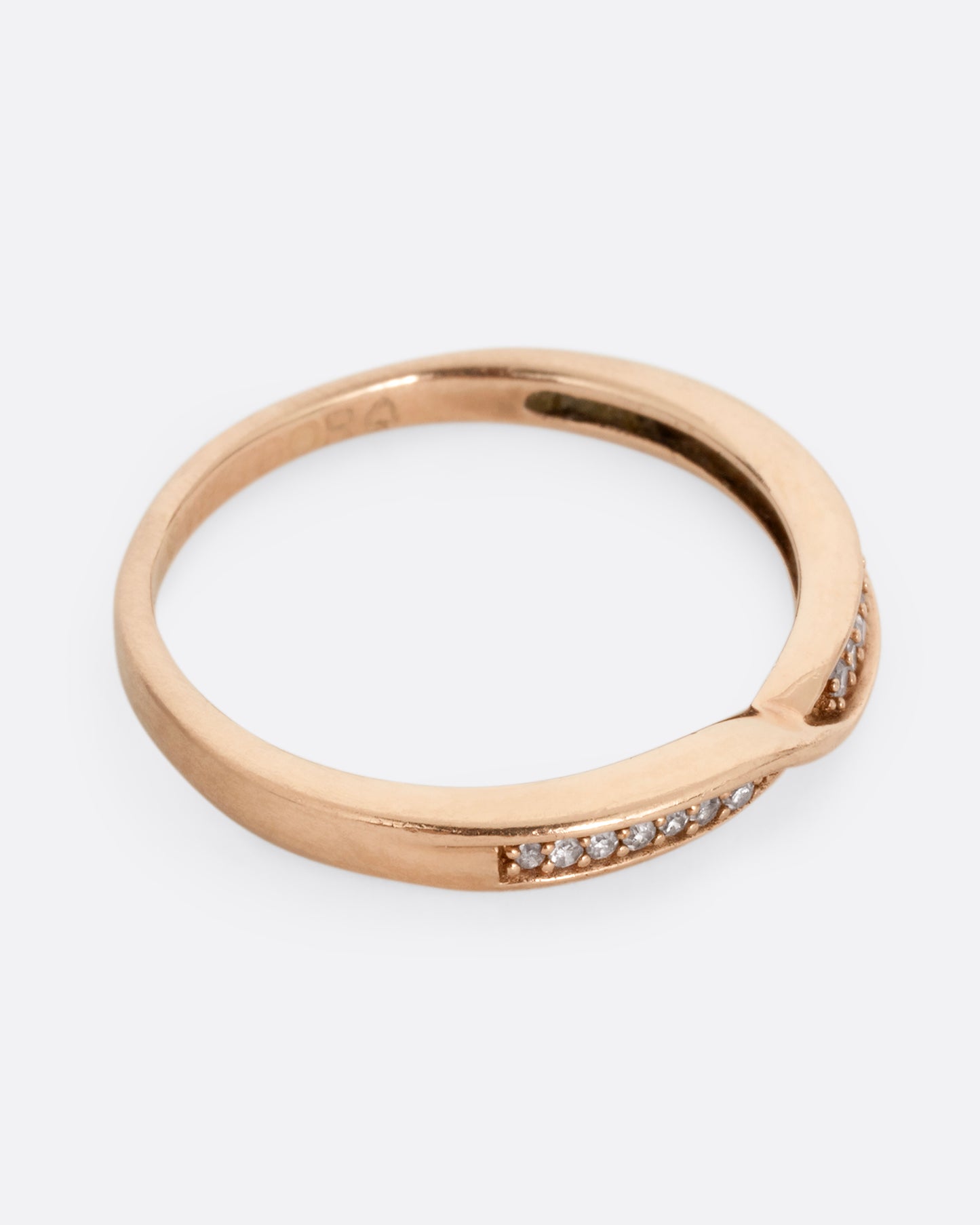 A rose gold ring with a twist at the center and seven white diamonds on either side. Shown from the side.