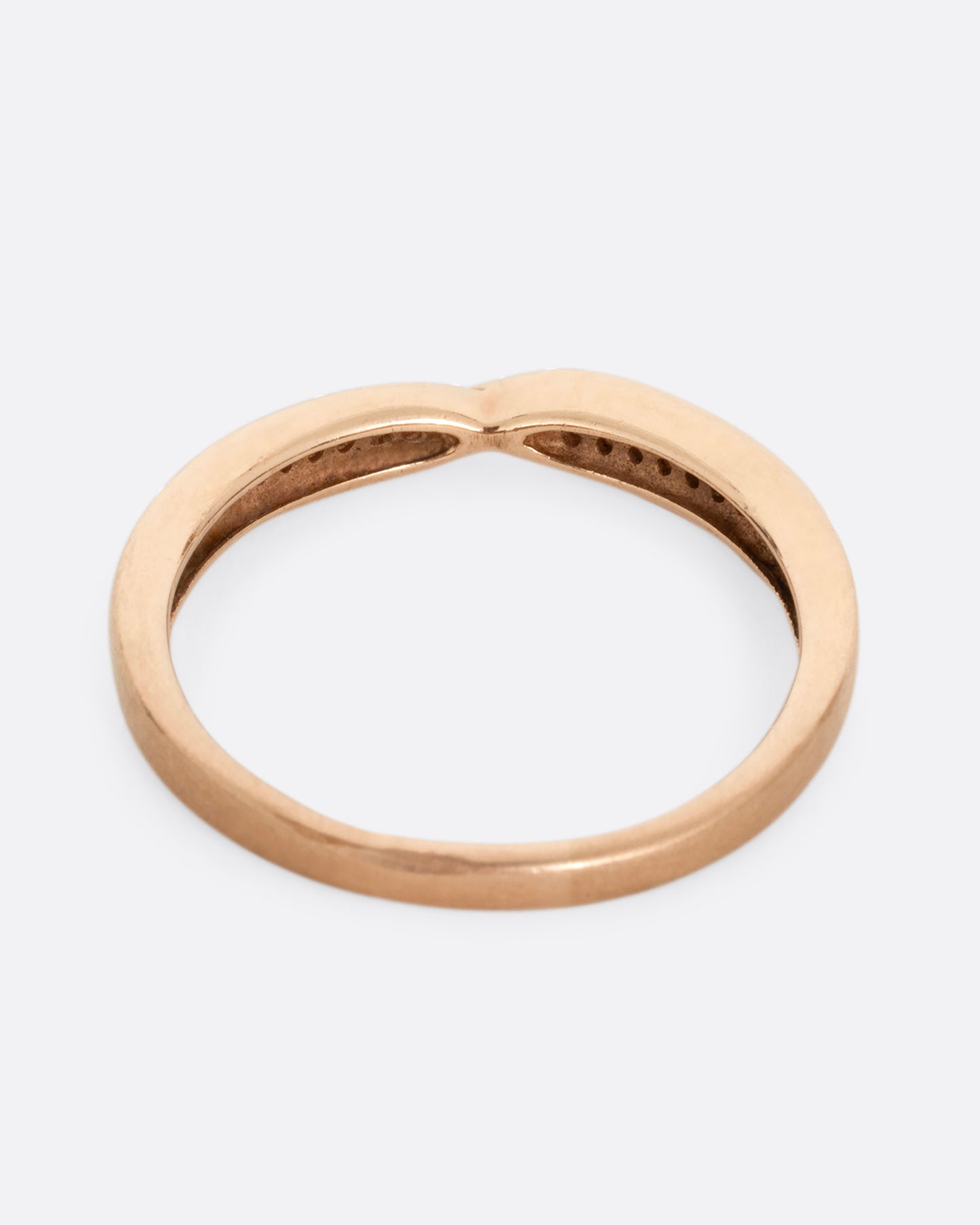 A rose gold ring with a twist at the center and seven white diamonds on either side. Shown from the back.