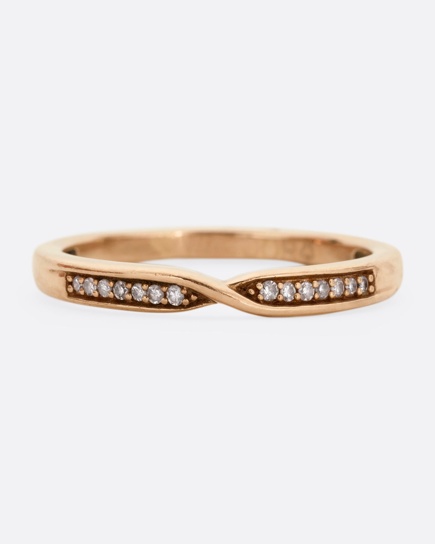 A rose gold ring with a twist at the center and seven white diamonds on either side. Shown from the front.