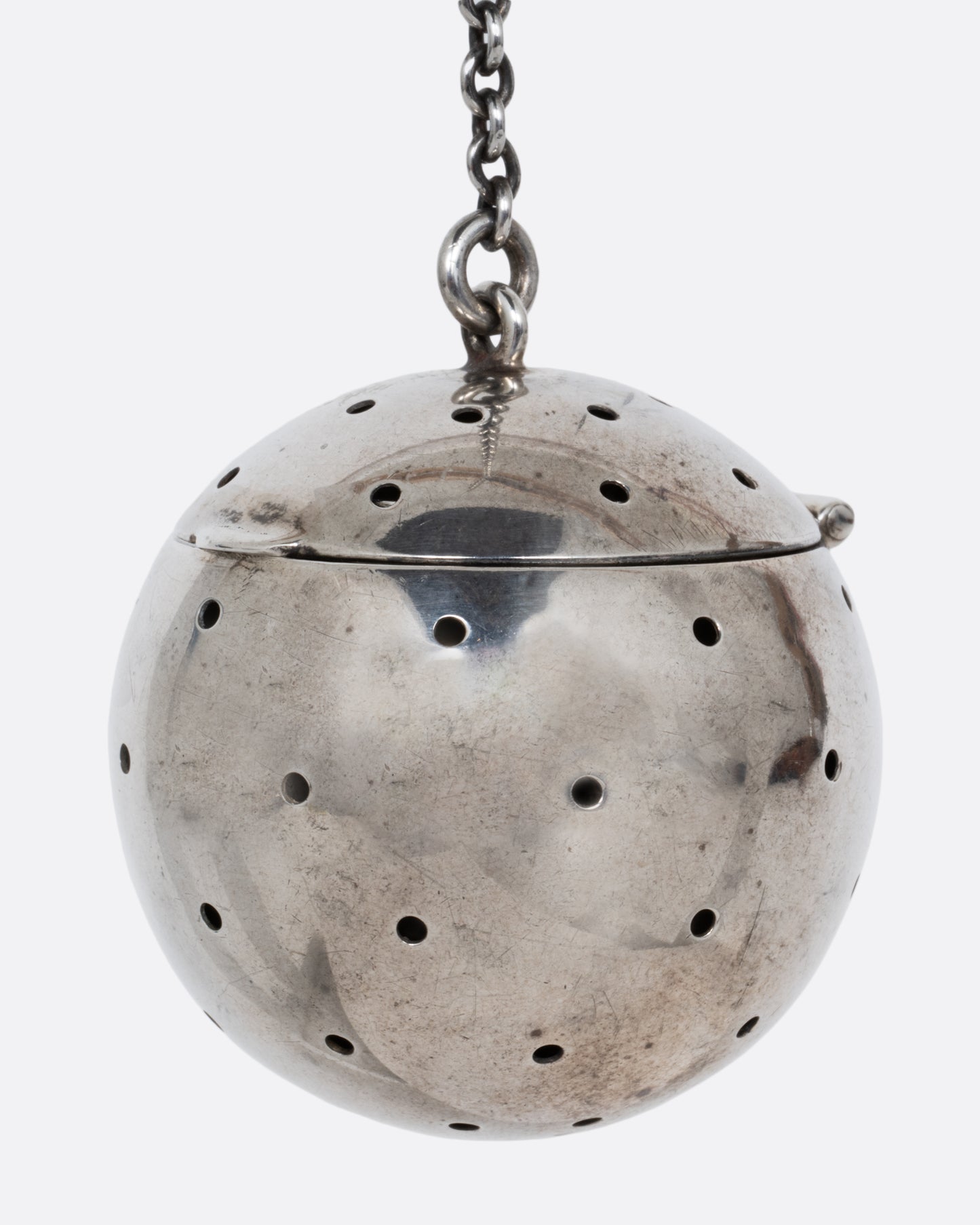 A silver spherical tea infuser topped with a hinged lid. Shown from the side.