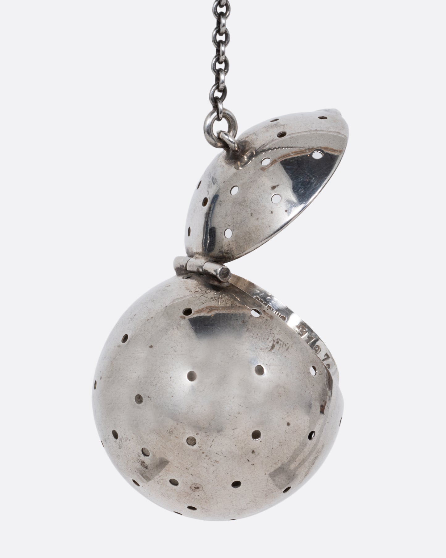 A silver spherical tea infuser topped with a hinged lid. Shown from the back.