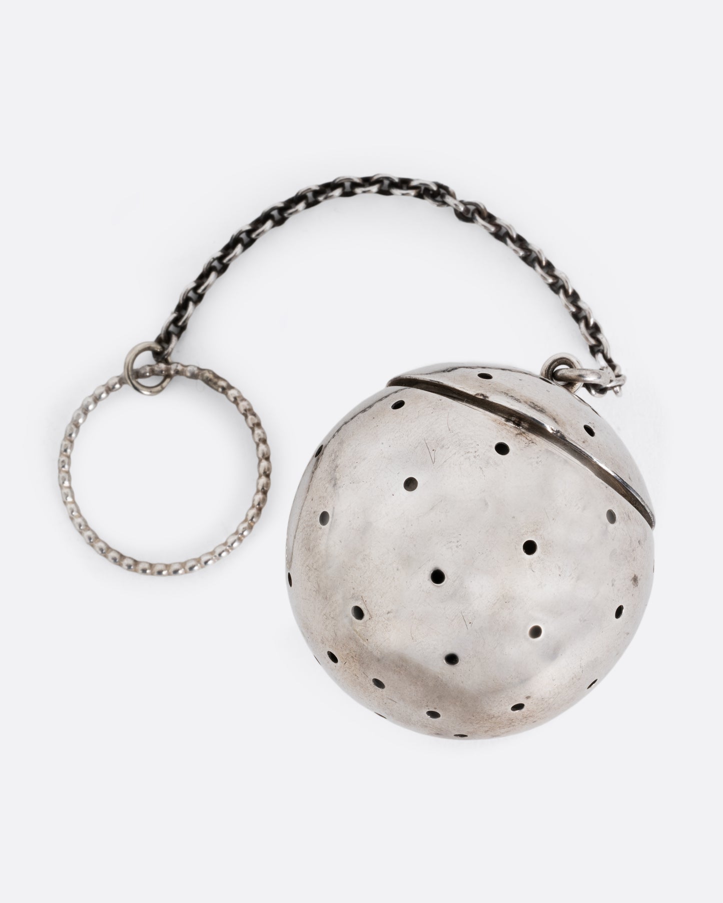 A silver spherical tea infuser topped with a hinged lid. Shown lying flat from the front.
