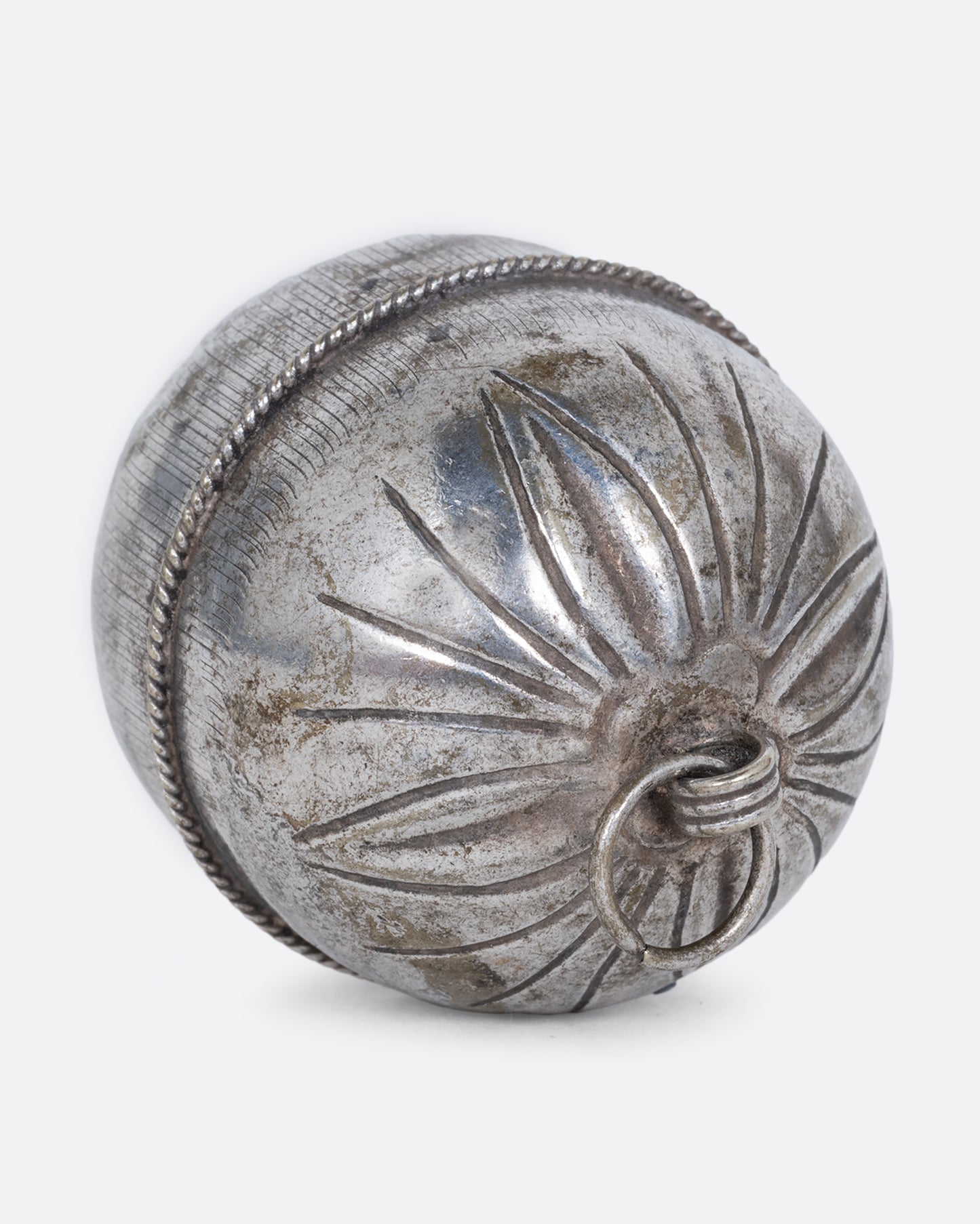 A silver engraved bell charm. Shown lying on its side from the top.