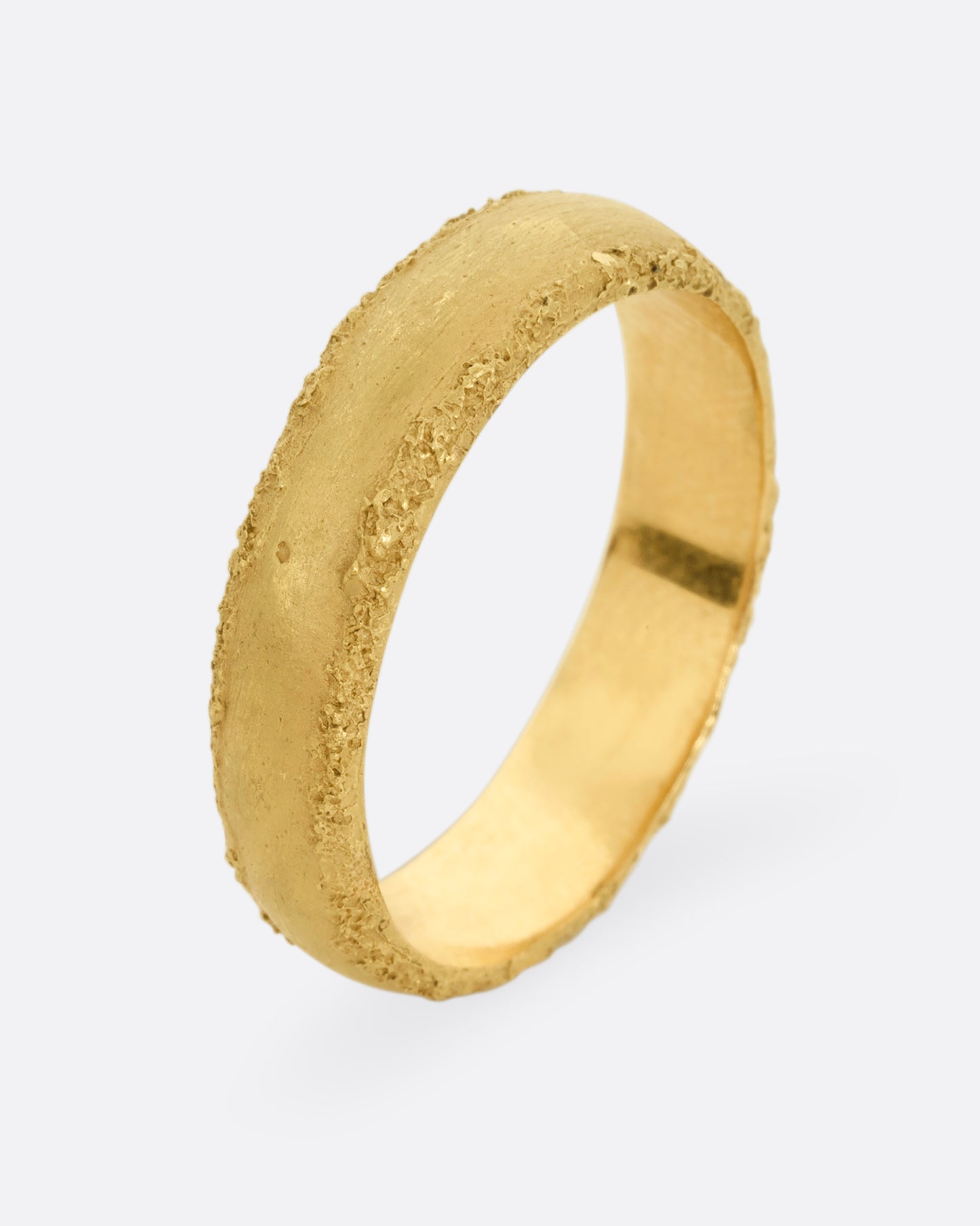 A yellow gold band with a matte center and textured edges. Shown from the side, standing up.