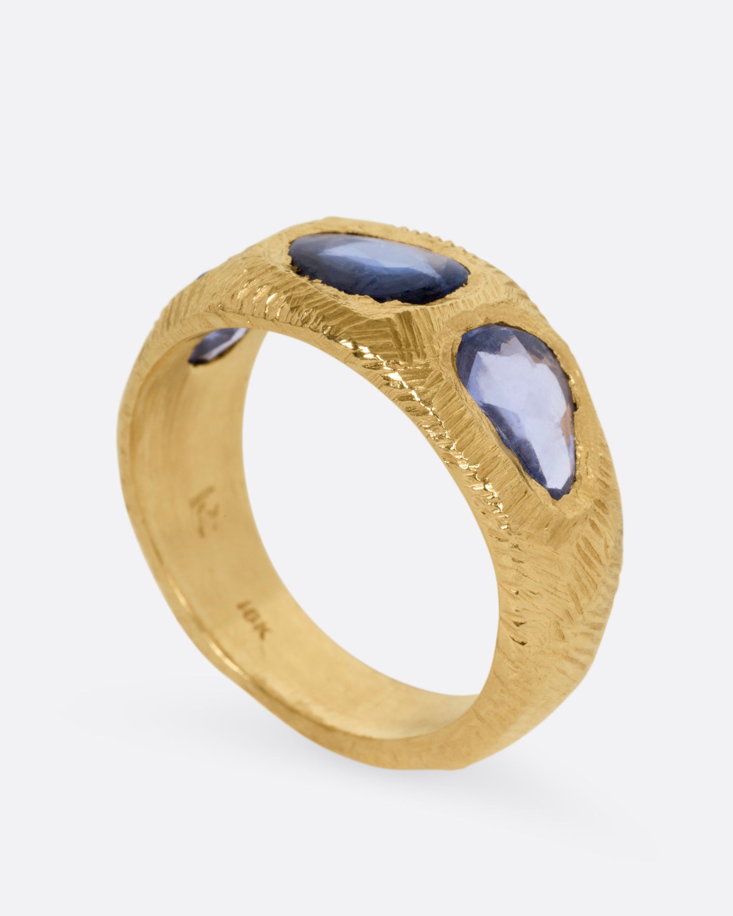 A yellow gold ring with three blue sapphires, shown standing up from the side.