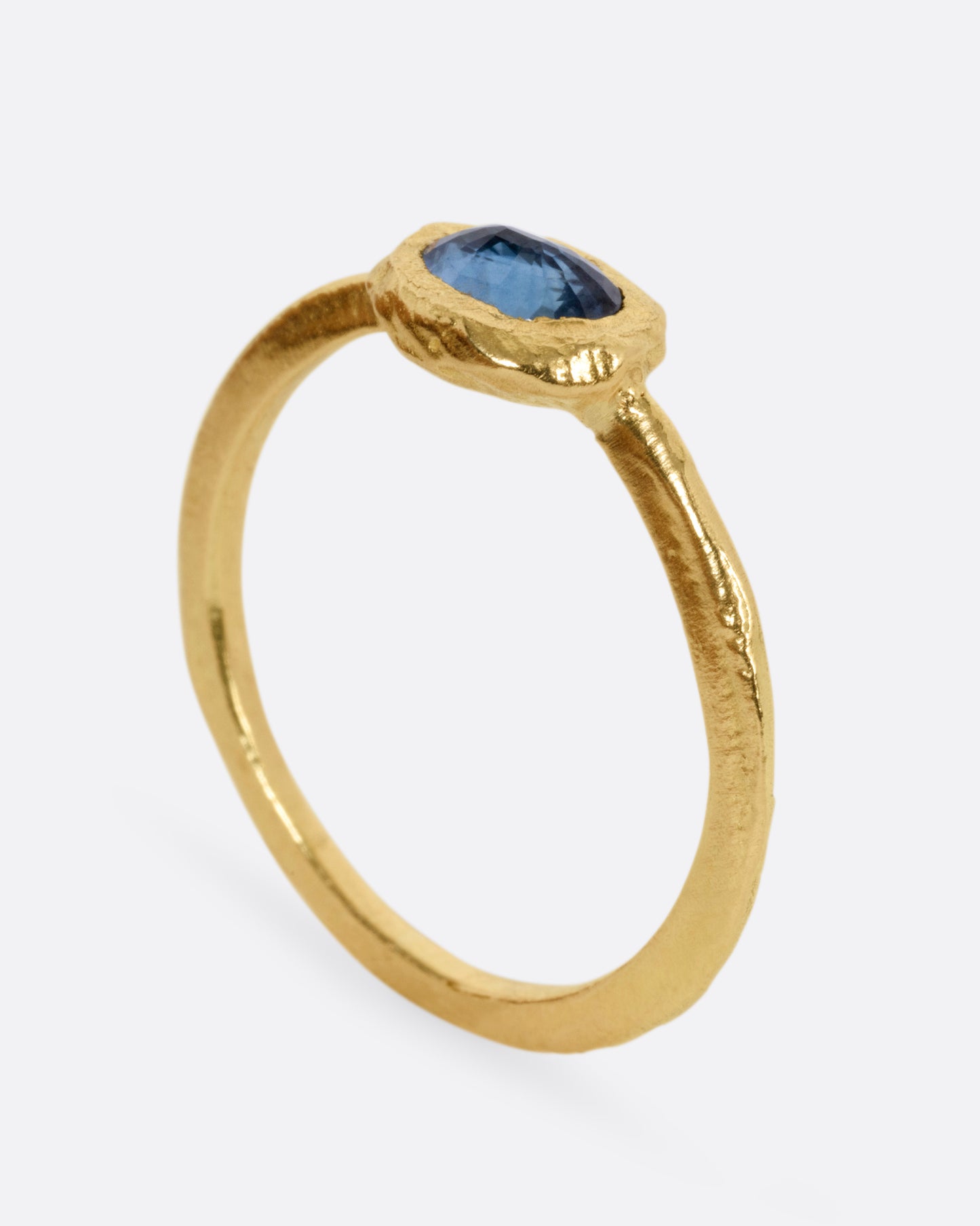 A yellow gold ring with a blue sapphire, shown from the side standing up.