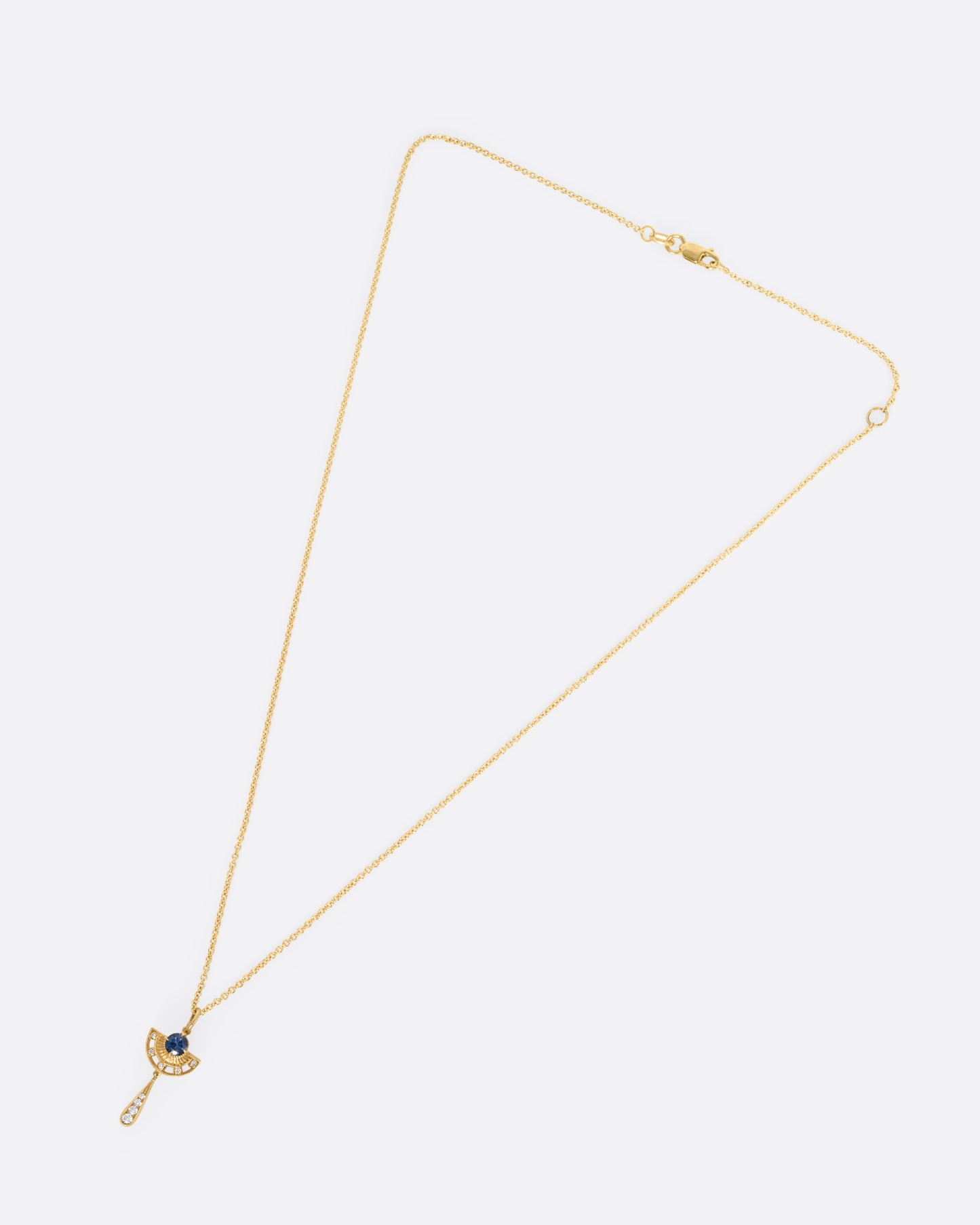 A yellow gold necklace with a sapphire and diamond pendant with open cutouts and a dangle drop. Shown from the front.