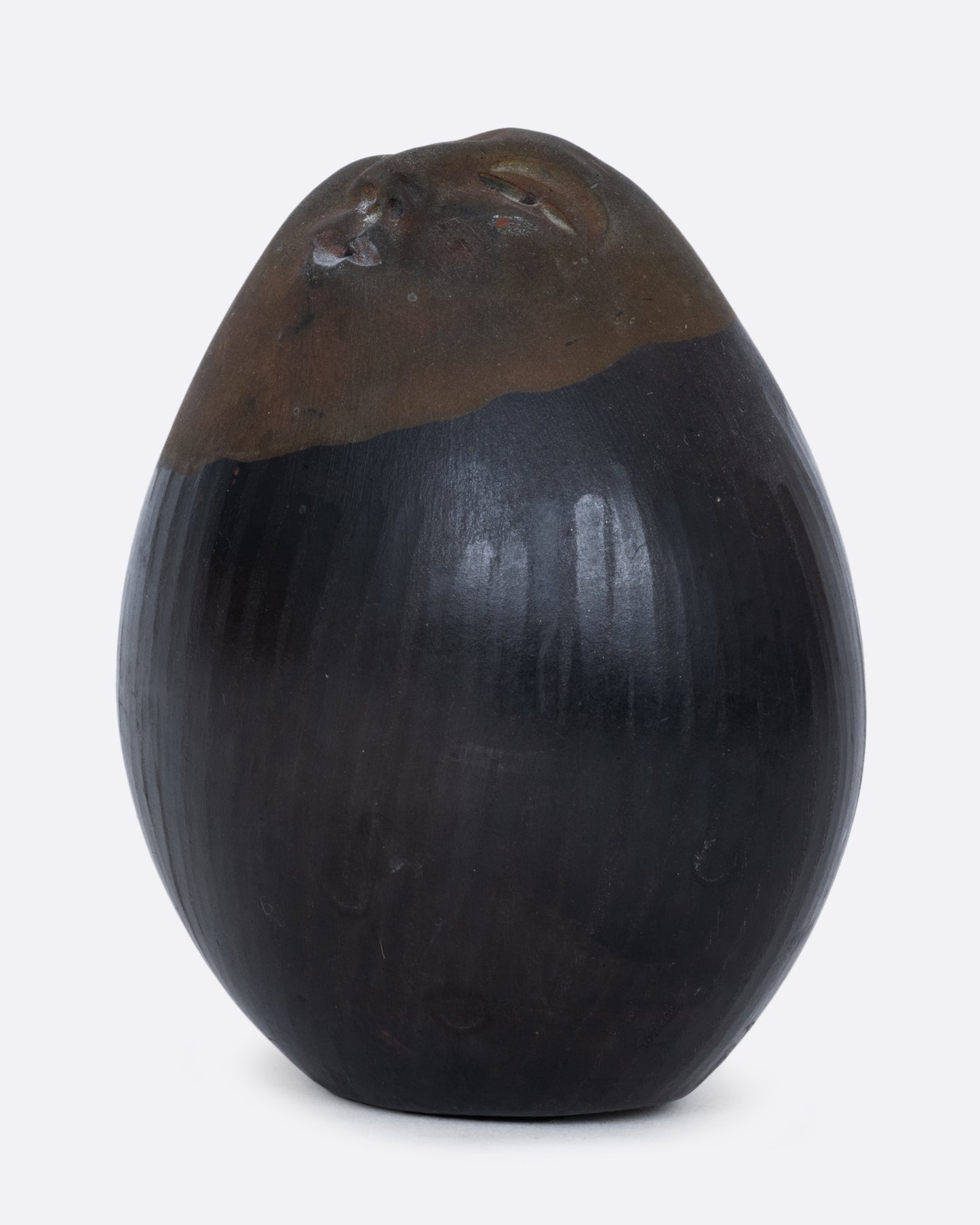 A black and brown egg-shaped rattle with a face carved on one end, shown from the side.