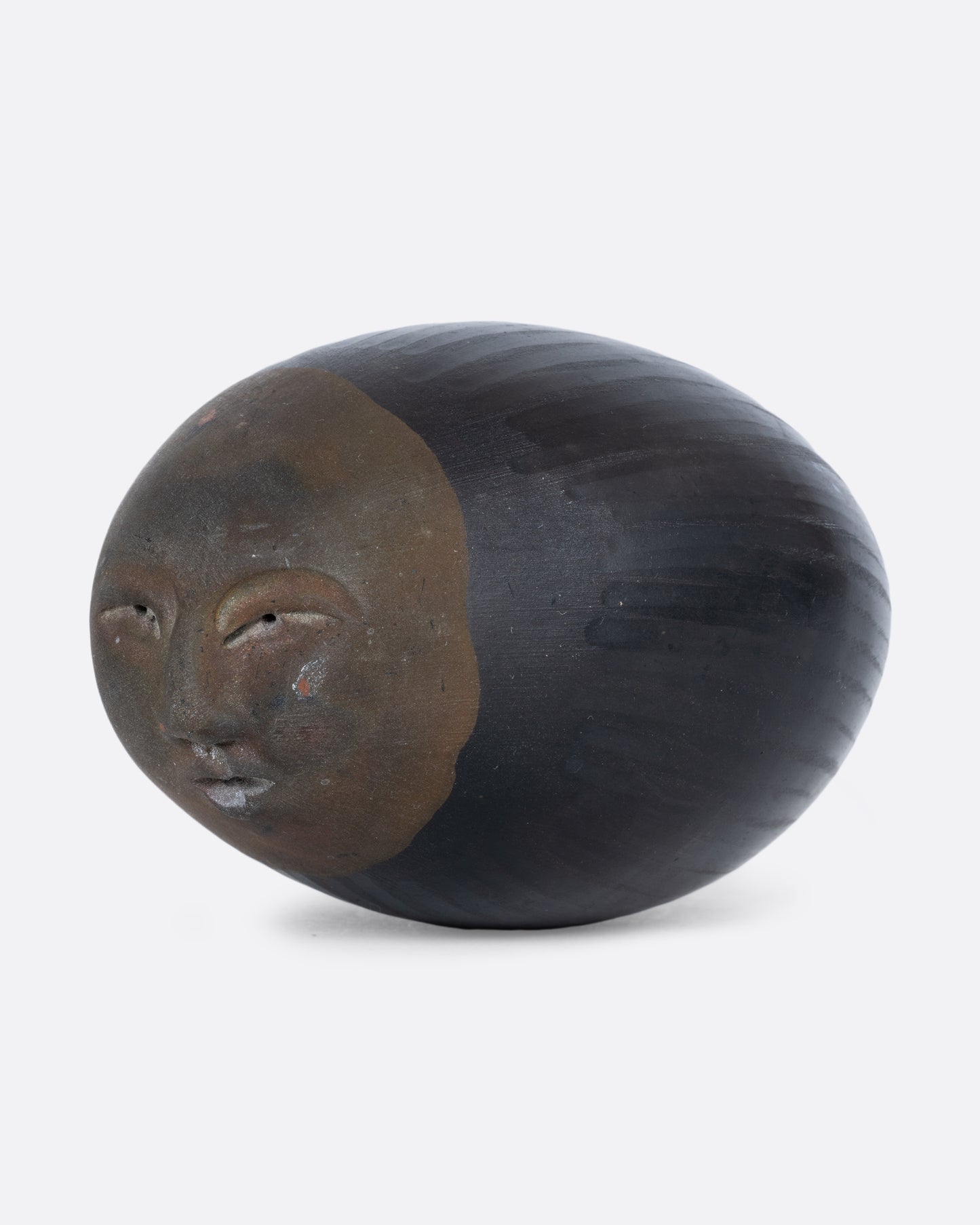 A black and brown egg-shaped rattle with a face carved on one end, shown on its side from the top.