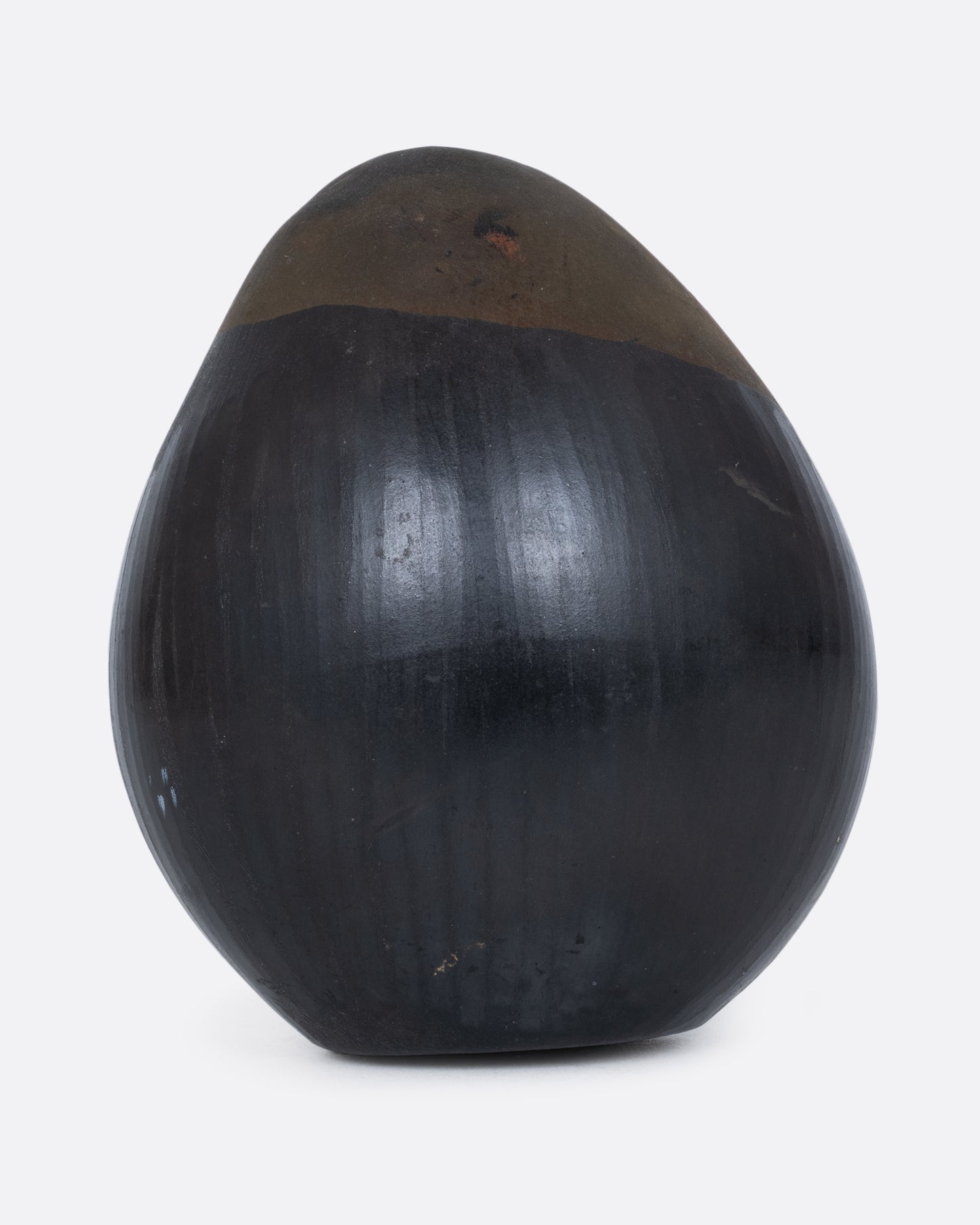 A black and brown egg-shaped rattle with a face carved on one end, shown from the back.