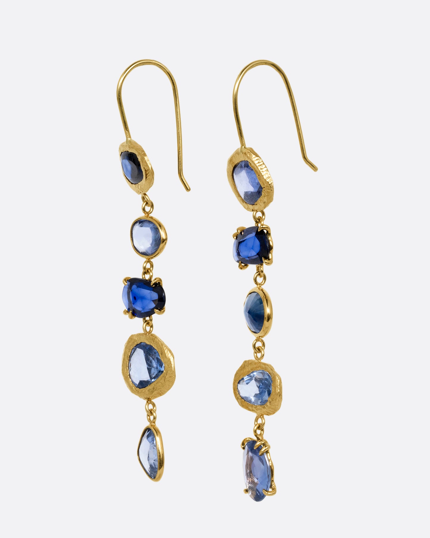 A pair of yellow gold dangle earrings with a cascade of blue rose cut sapphires with a mix of hand carved, bezel, and prong settings. Shown from the side.