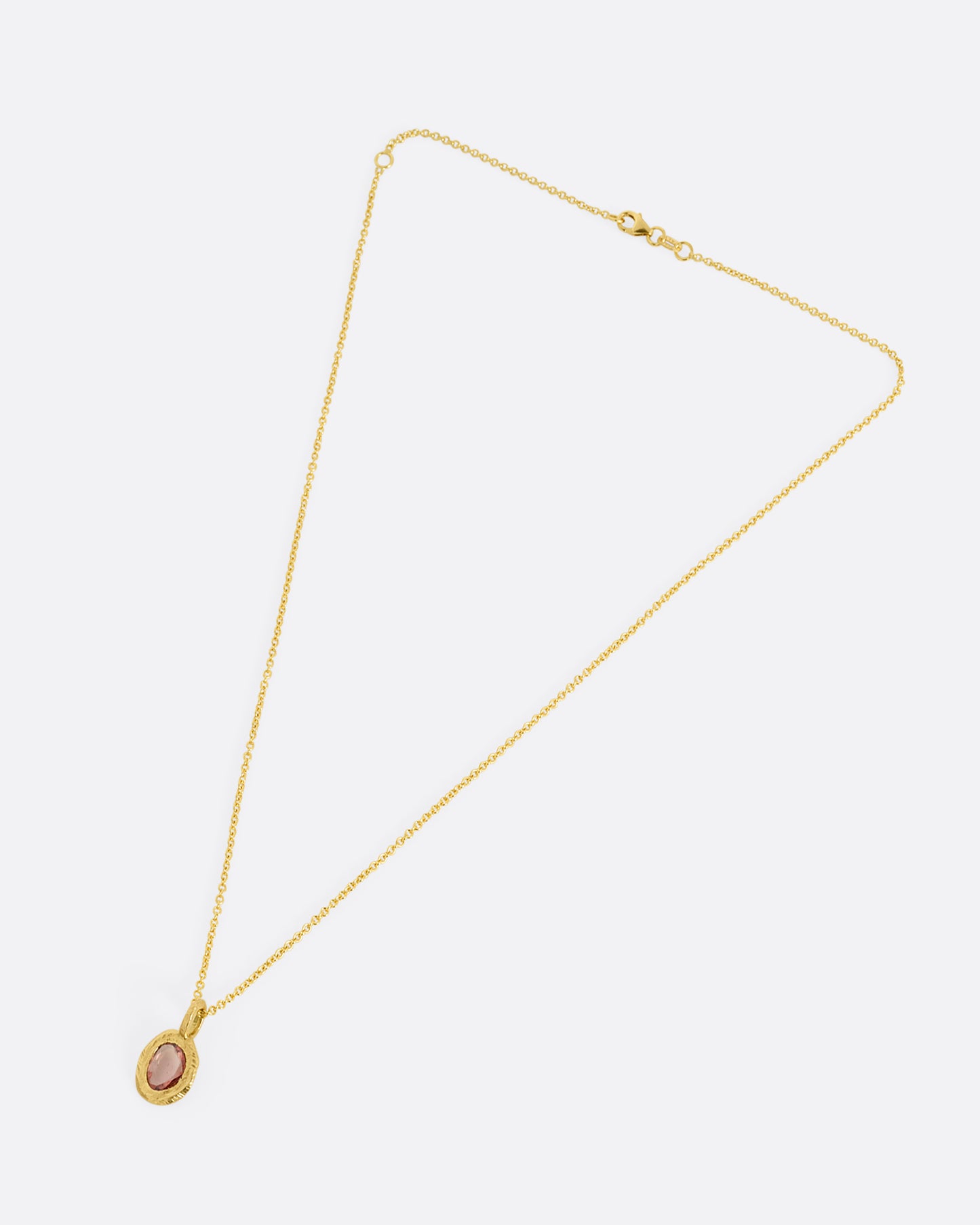 A yellow gold cable chain with a pendant with a burgundy sapphire, shown from the front
