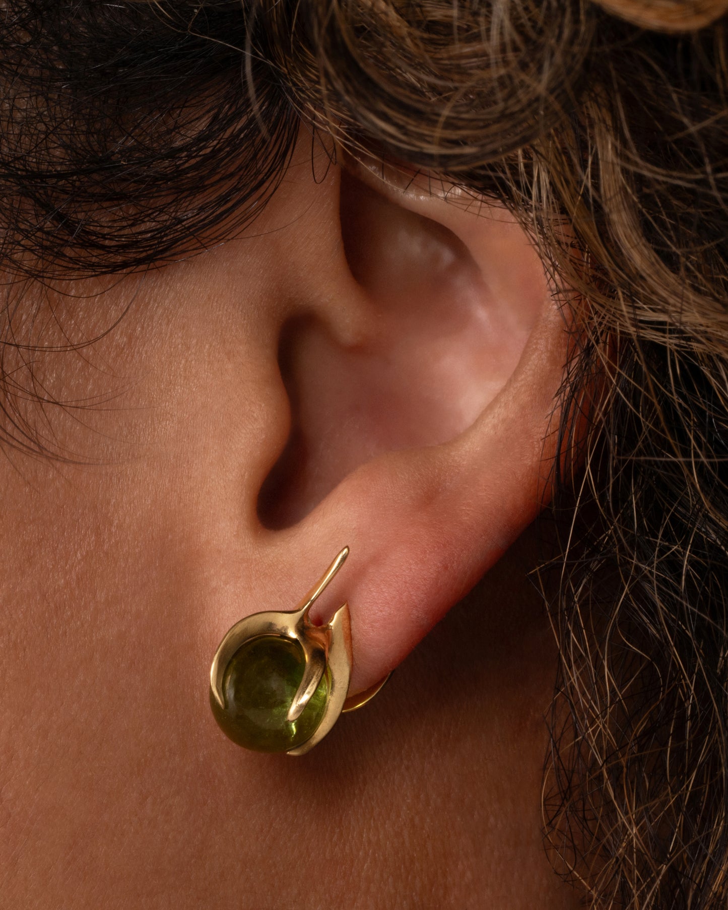 A pair of yellow gold stud earrings with green tourmaline spheres set in flame-like settings. Shown on an ear.