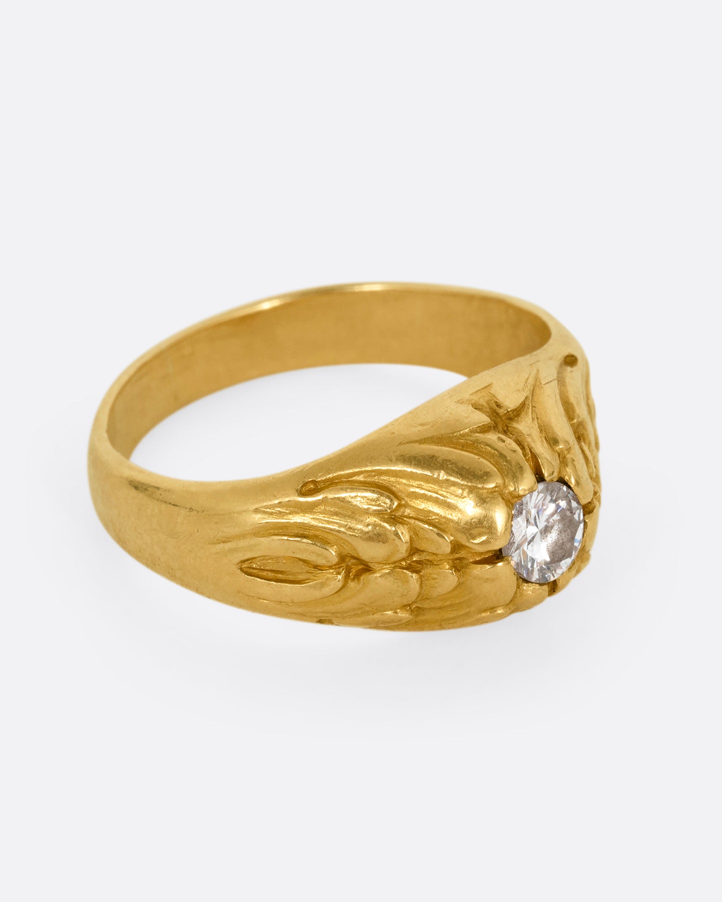 A yellow gold dome ring with textural waves on its top and a round central diamond. Shown from the side.