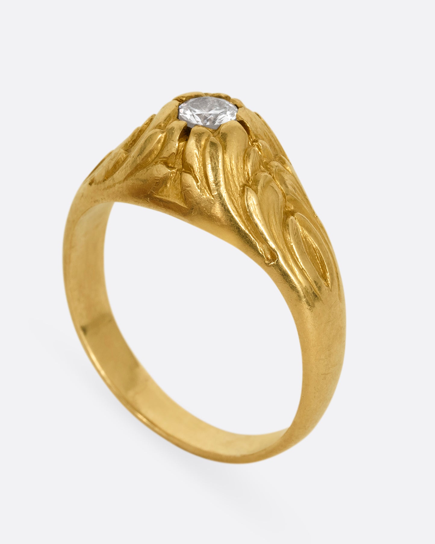 A yellow gold dome ring with textural waves on its top and a round central diamond. Shown standing up from the side.