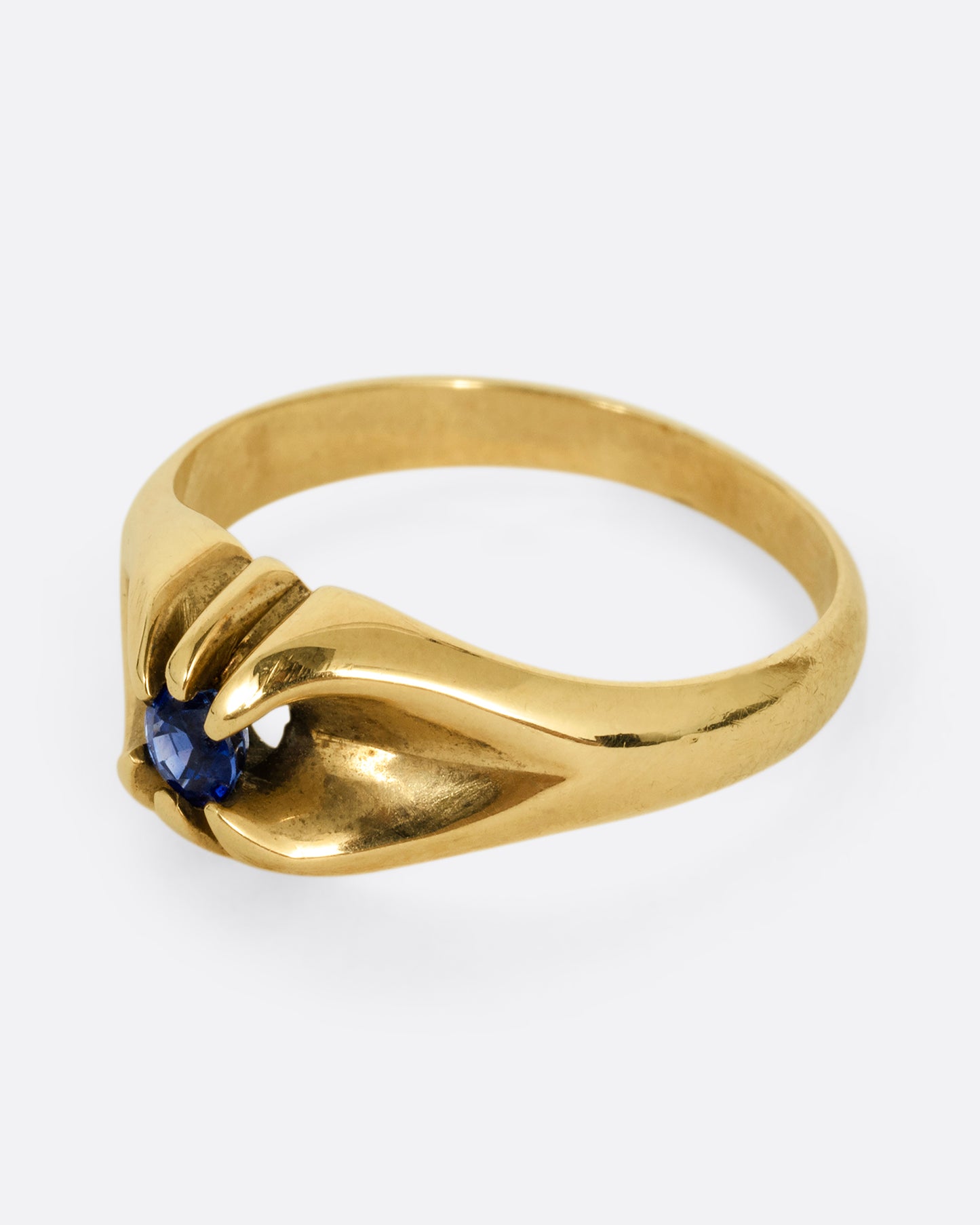 A yellow gold ring with a prong set blue sapphire. Shown from the side.