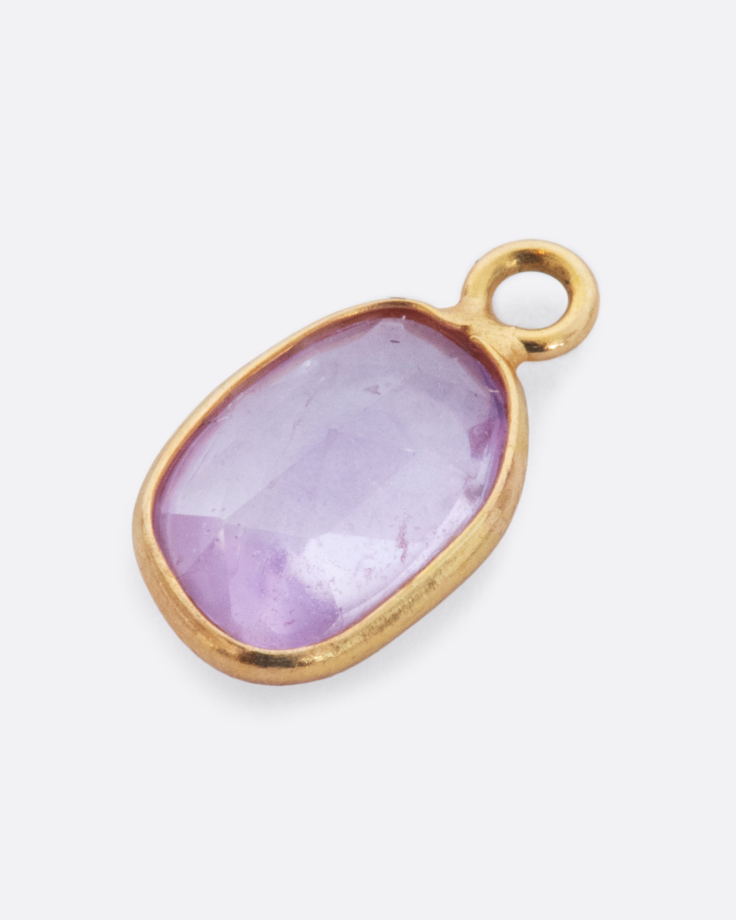 A pink sapphire slice dangle set in yellow gold with a yellow gold bail. Shown lying flat from the front.