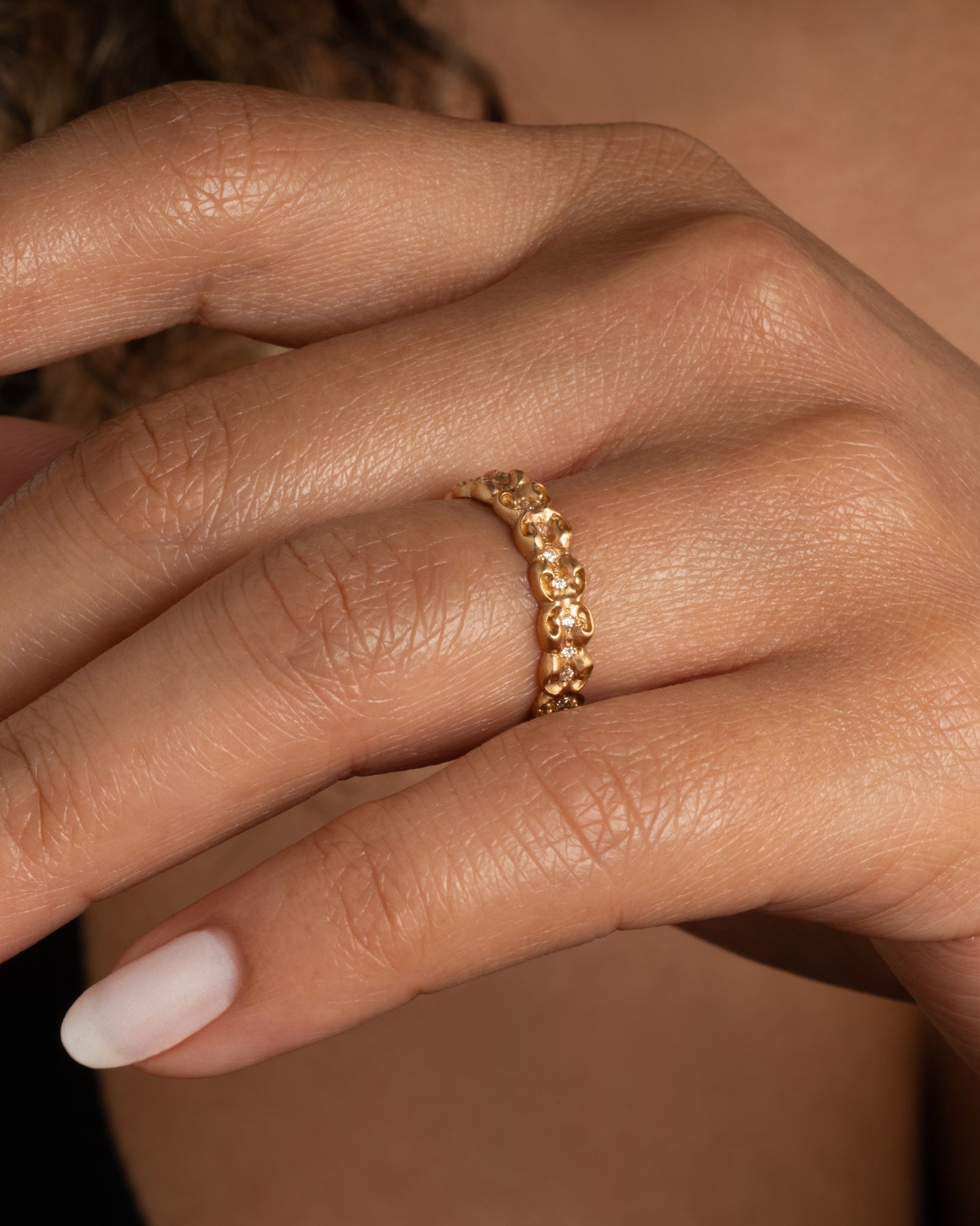 A bubble floral infinity band with round white diamonds all the way around. Shown worn on a finger.