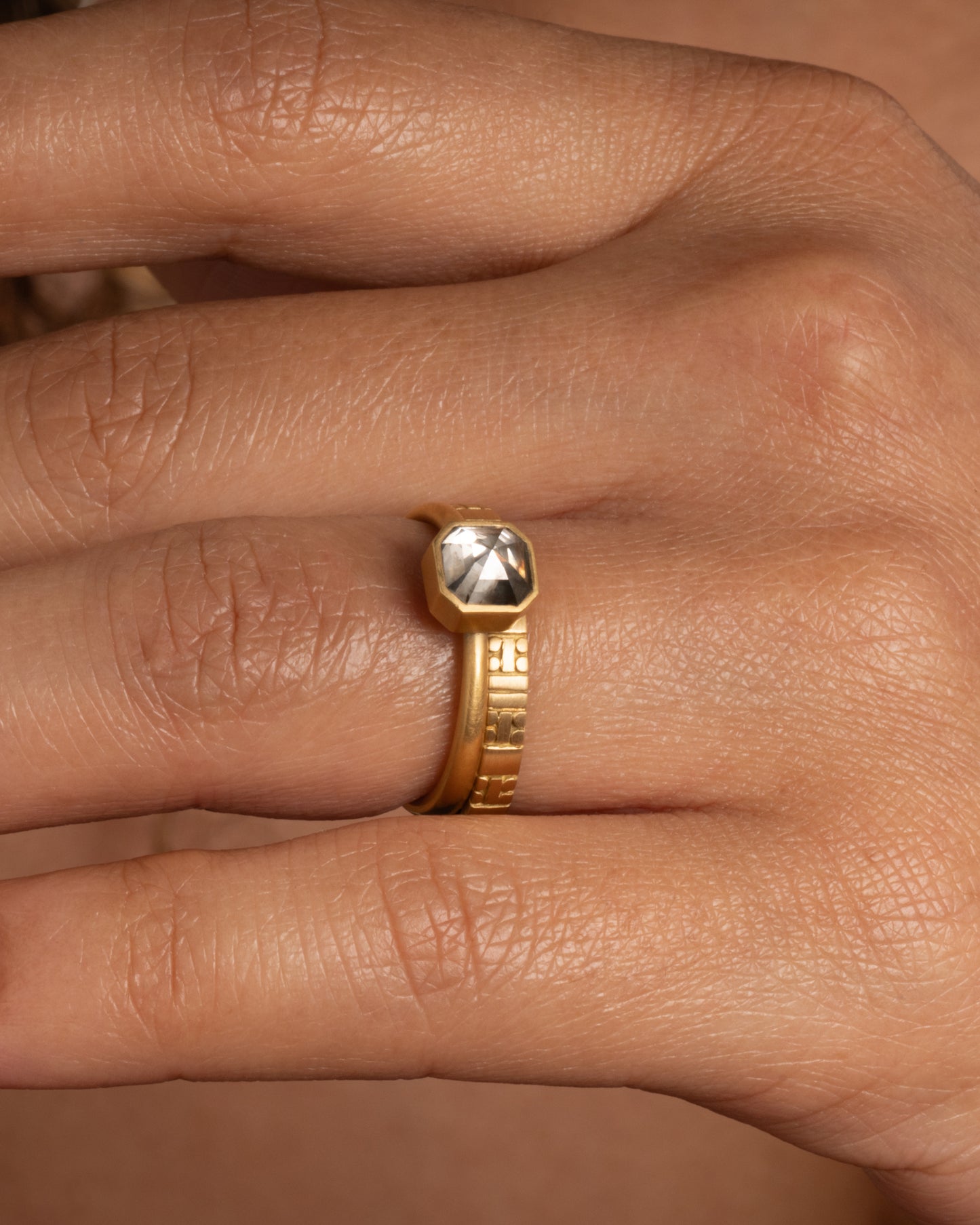 A yellow gold ring with a smokey octagonal diamond. Shown worn on a finger stacked with a geometric yellow gold band.
