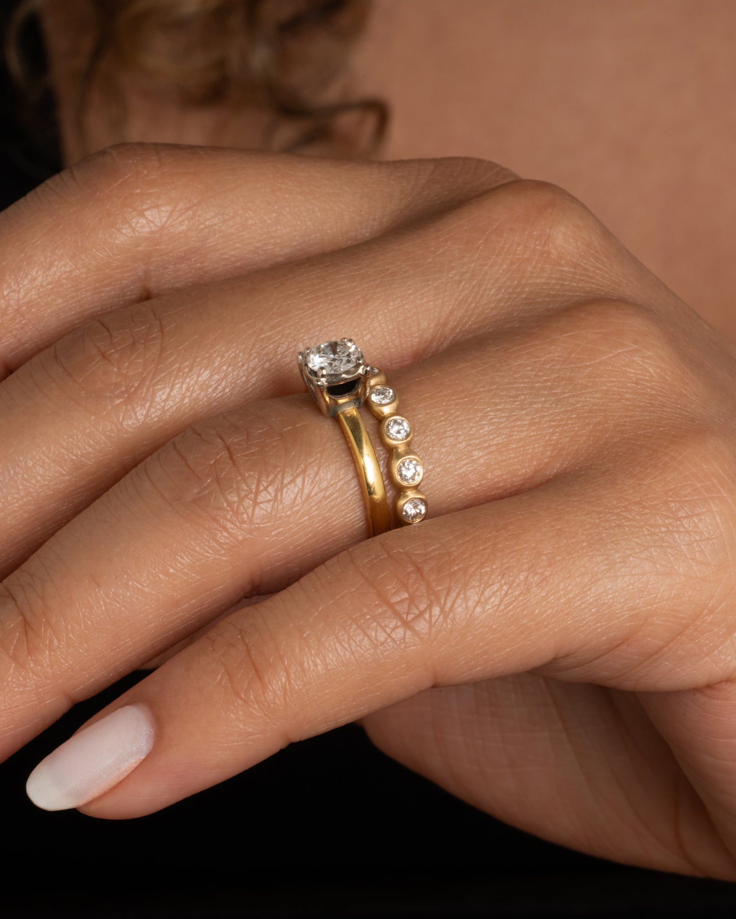 An eternity band of bezel set white diamonds in matte gold settings. Shown worn on a finger paired with a vintage engagement ring.